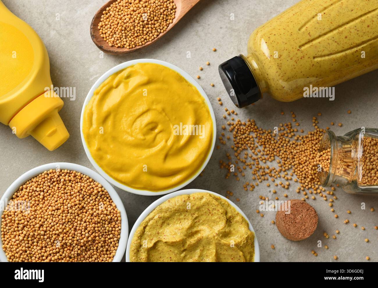 Adagiare in piano due bottiglie diverse di mostarde in caramelle con le bottiglie di plastica e i semi di senape. Nessuna etichetta sulle bottiglie. Foto Stock