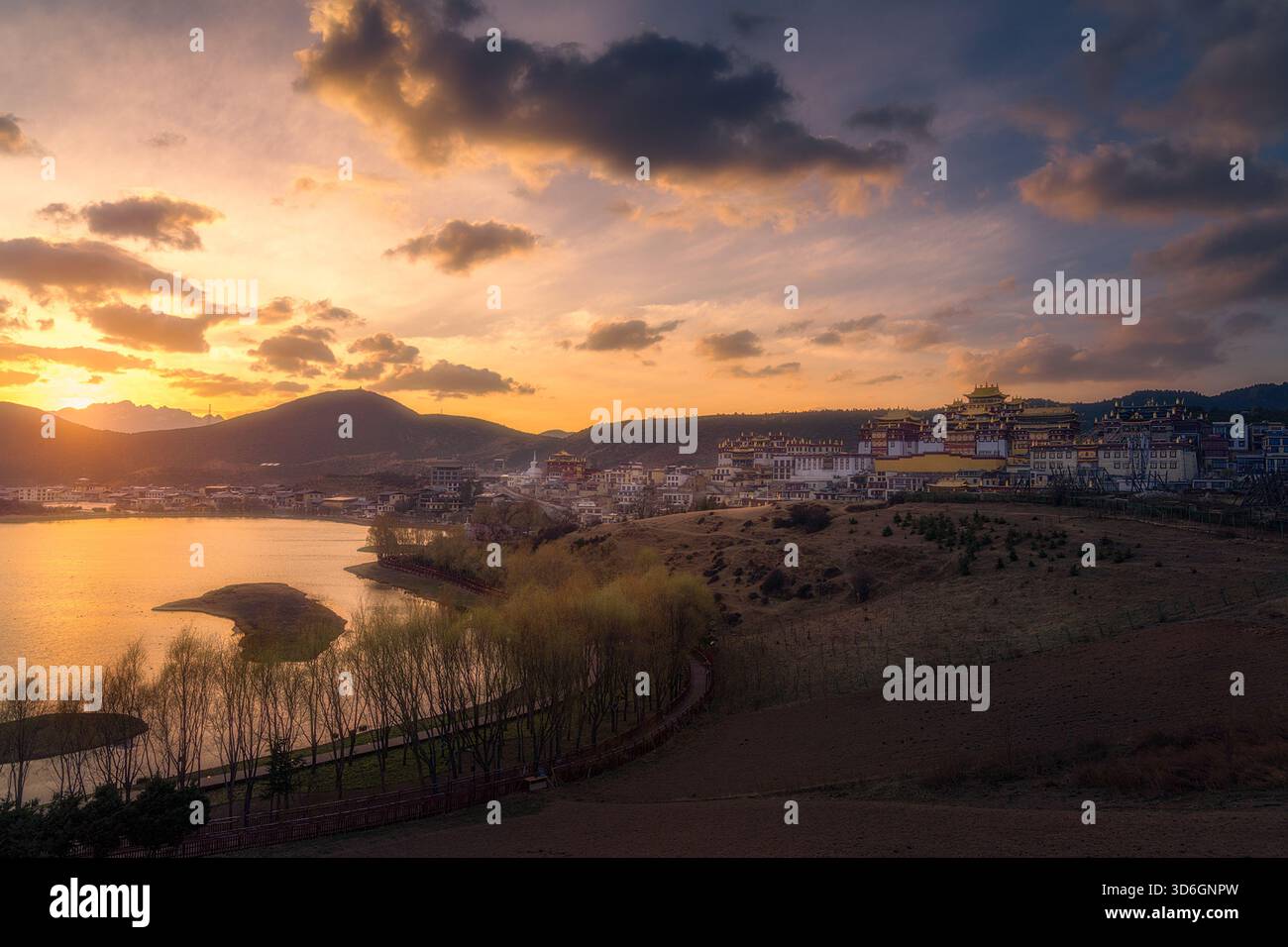 Vista di un tranquillo lago che riflette il tramonto dorato mentre bacia l'orizzonte vicino a un villaggio tibetano, la prefettura autonoma tibetana di Diqing, Yunnan, Chin Foto Stock