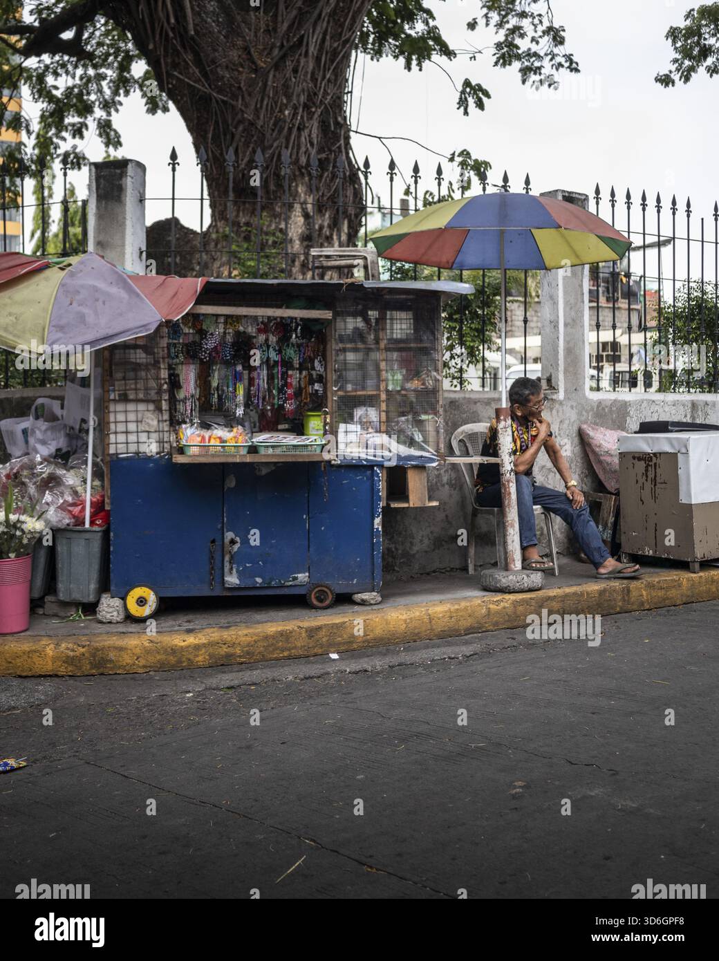 Manila, Filippine - 15 maggio 2023: Veduta di una vivace banchina di venditori di strada blu, piena di merci colorate, ancorata da un albero e castin Foto Stock