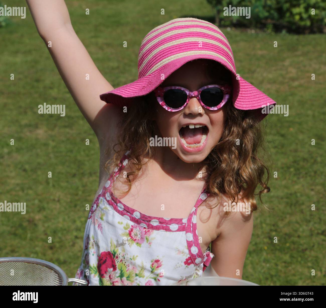 Ritratto di una bambina di sette anni che indossa occhiali da sole e cappello da sole in un giardino nel Surrey in Inghilterra Foto Stock