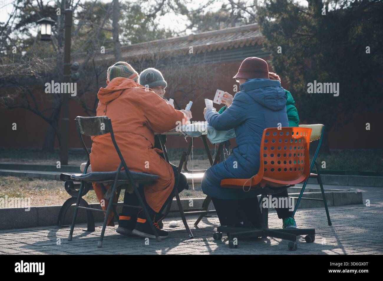 Il sole e le carte invernali in un parco di Pechino, mentre le donne anziane condividono calore e una partita pomeridiana lenta Foto Stock