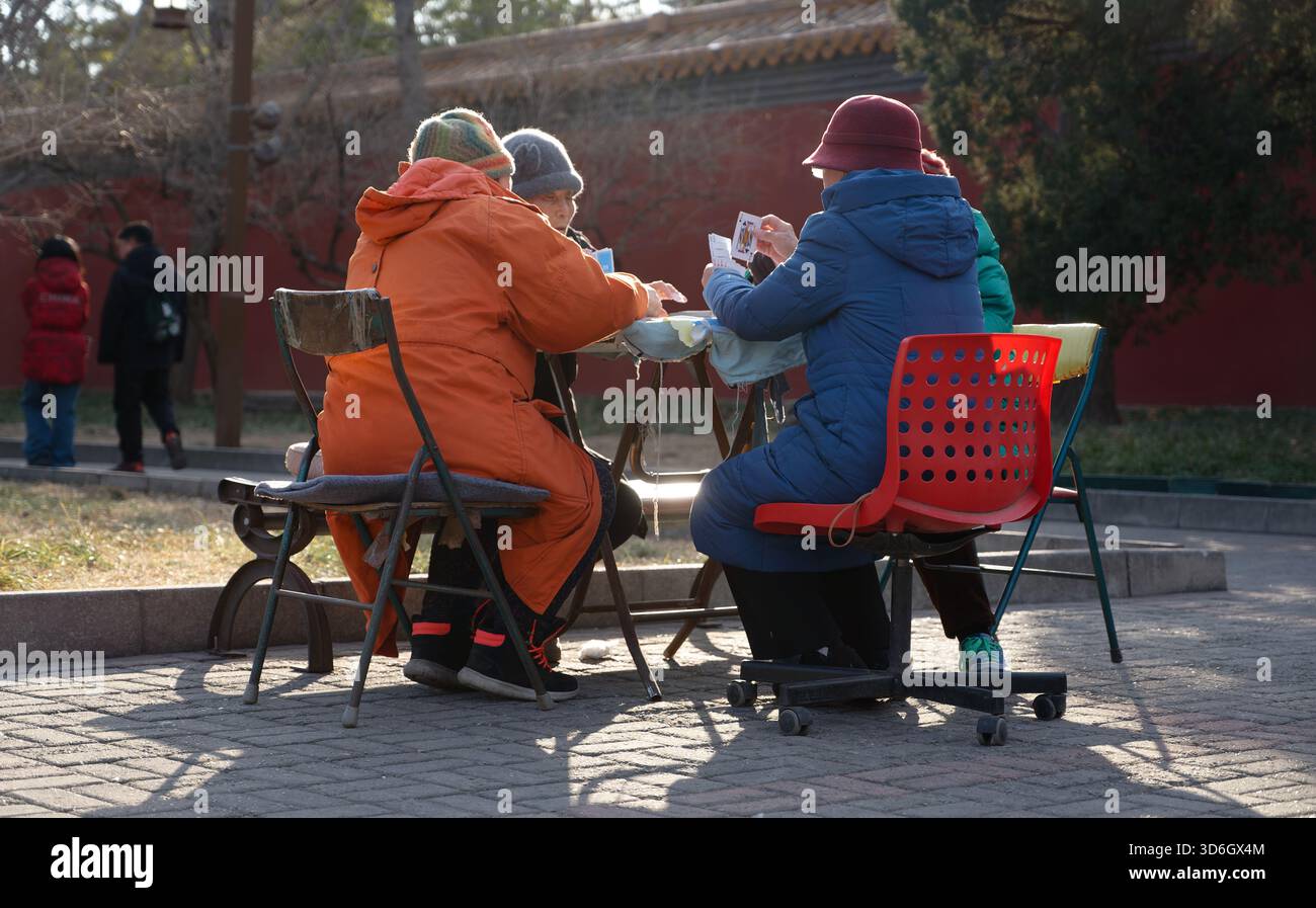 Il sole e le carte invernali in un parco di Pechino, mentre le donne anziane condividono calore e una partita pomeridiana lenta Foto Stock