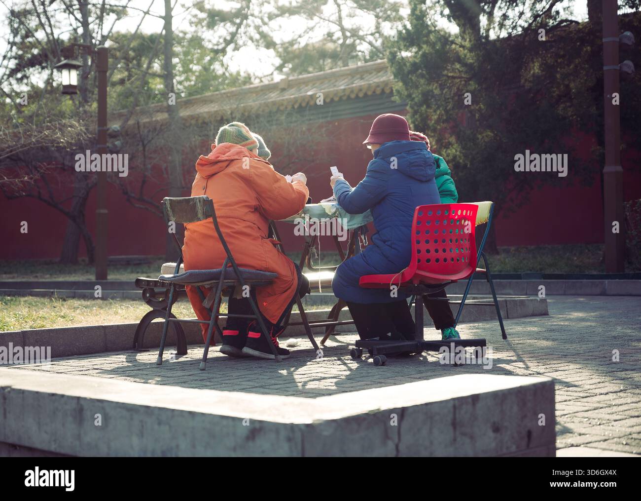 Il sole e le carte invernali in un parco di Pechino, mentre le donne anziane condividono calore e una partita pomeridiana lenta Foto Stock