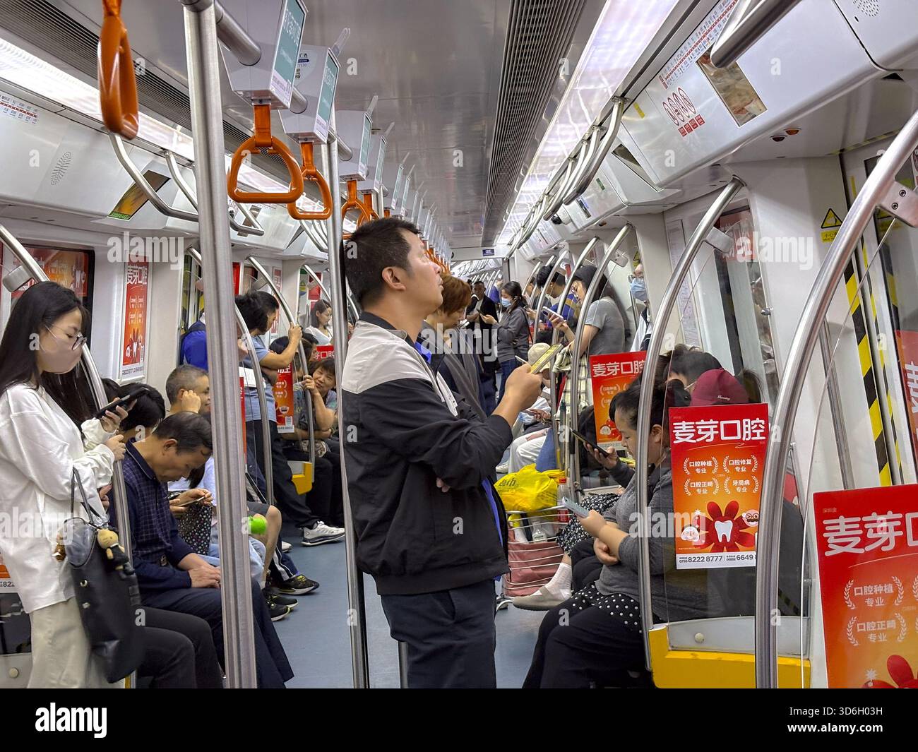 L'interno del treno della metropolitana di Shenzhen con pendolari in piedi e seduti, molti guardano i telefoni. Questa immagine cattura la vita urbana quotidiana e i trasporti pubblici Foto Stock