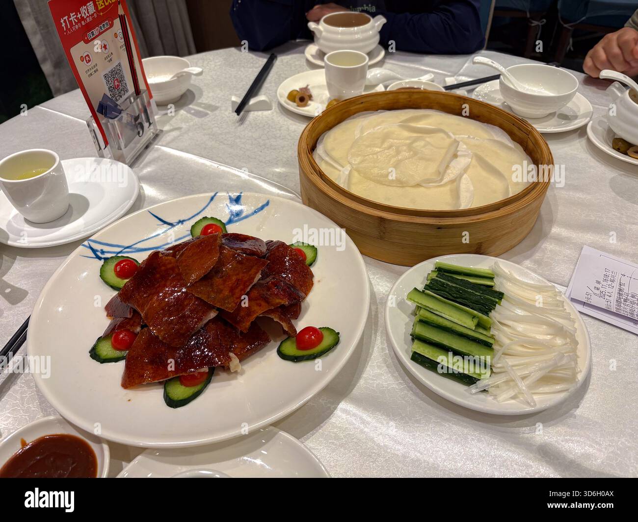 Anatra a fette di Pechino, servita con sottili pancake, cetriolo, cipolla primaverile e salsa hoisin su una tovaglia bianca in un tradizionale ambiente da ristorante. Foto Stock
