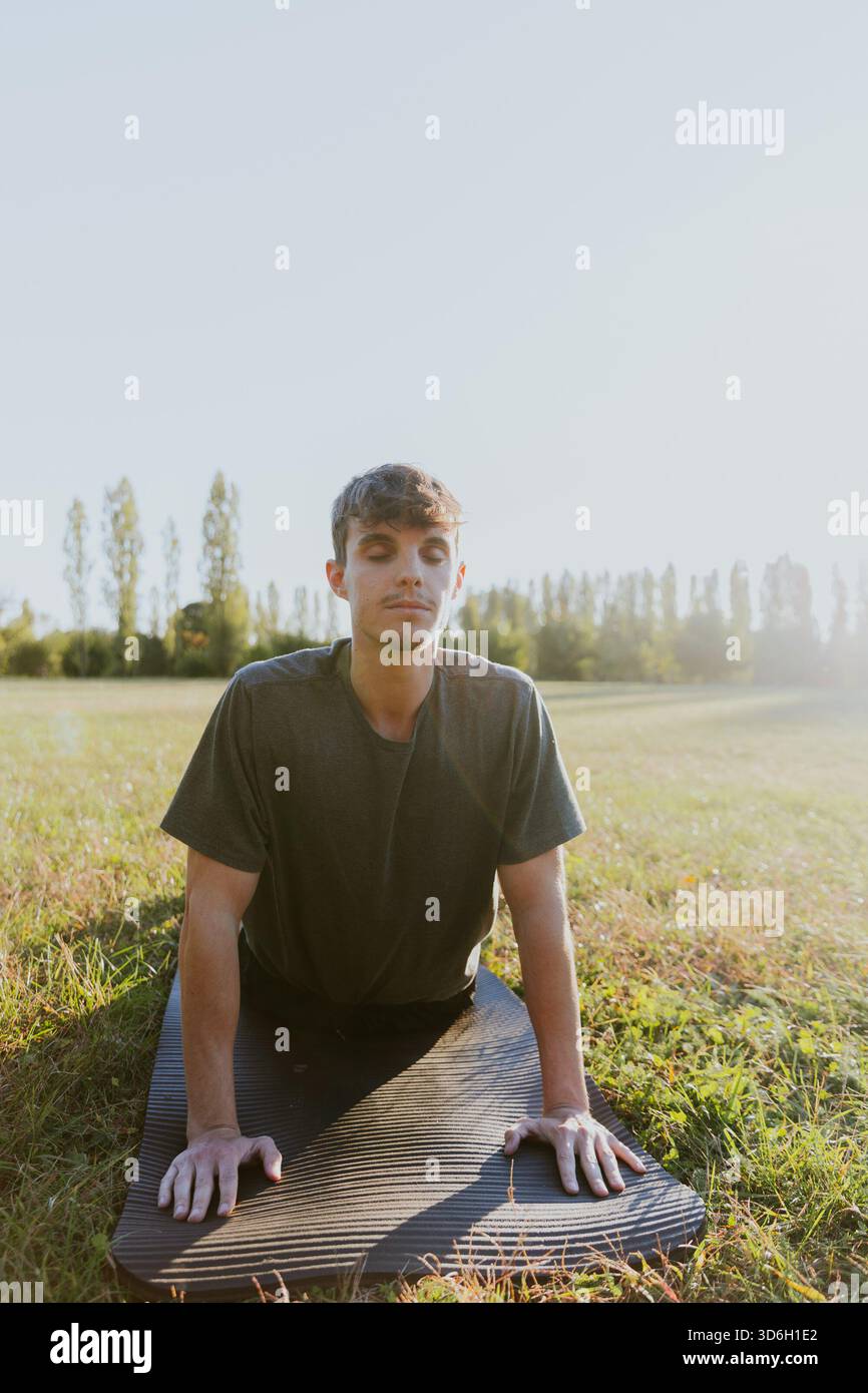 Un uomo sta facendo una posa di yoga su un tappetino in un campo. Concetto di calma e relax, poiché l'uomo si concentra sulla respirazione e sulla postura Foto Stock