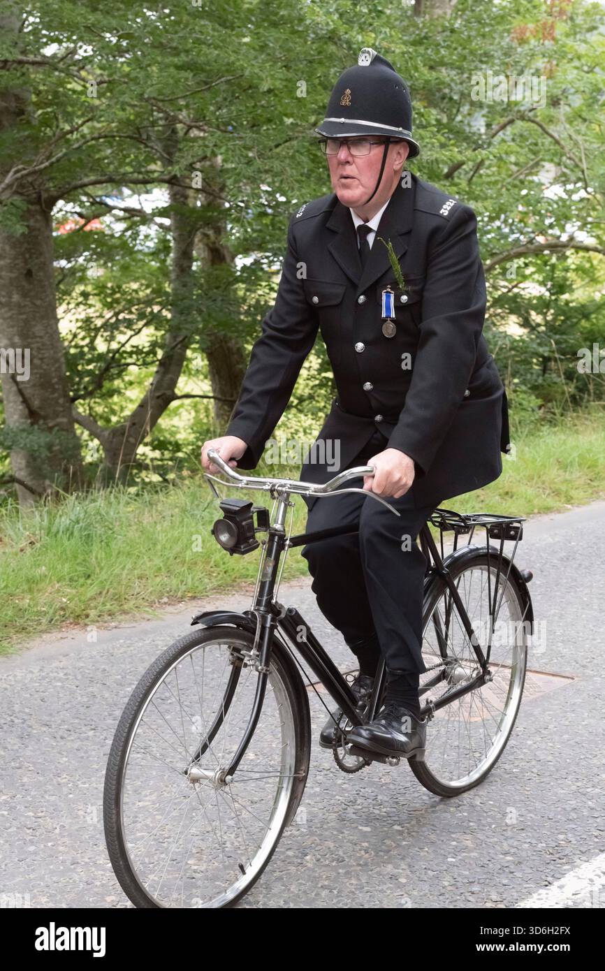 Bobby on the Bike, un poliziotto in pensione su una bicicletta della polizia d'epoca, che guida la marcia dei Lonach Highlanders durante la Lonach Highland Gathering Foto Stock