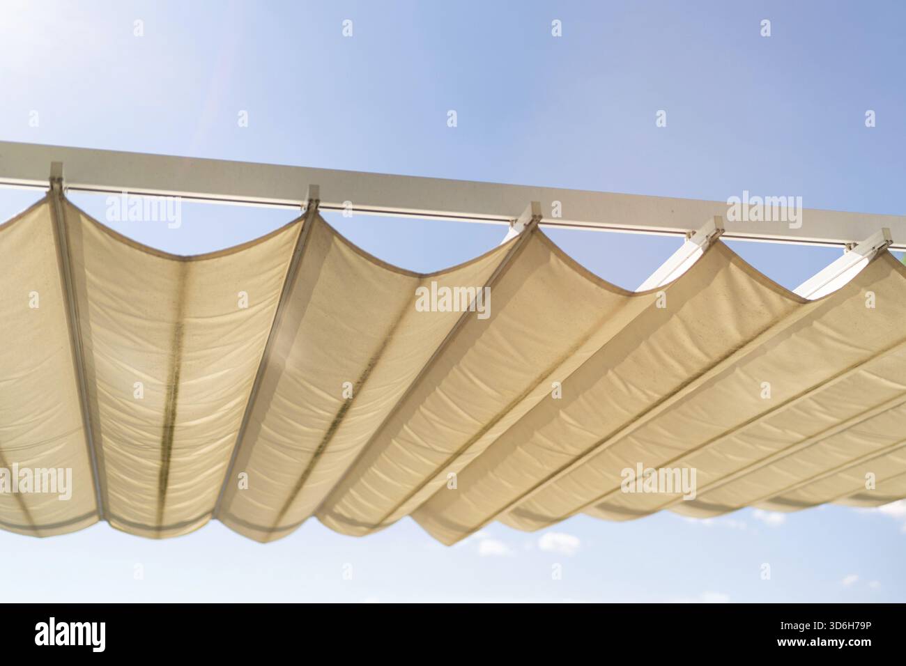 La tettoia in tessuto beige proietta ombre sotto la luce del sole, creando un gioco di luce e ombra. La struttura offre un riparo fresco e sereno Foto Stock