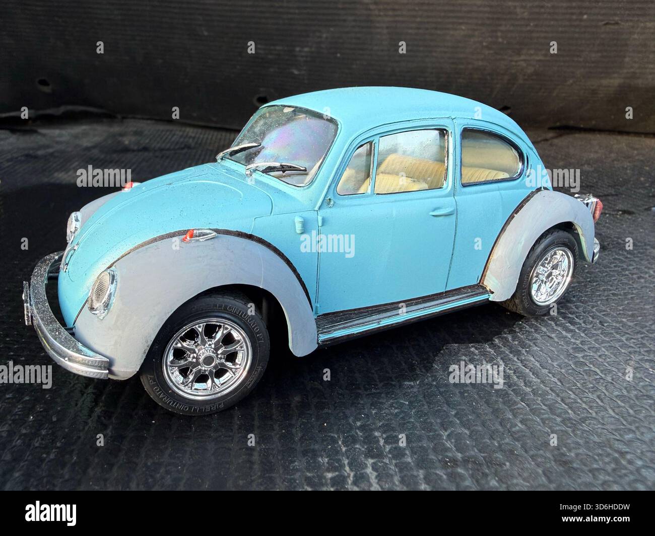 Primo piano di un modellino in scala di un'auto giocattolo vintage azzurra di un classico Maggiolino Volkswagen di tipo 1 su una superficie scura e testurizzata Foto Stock