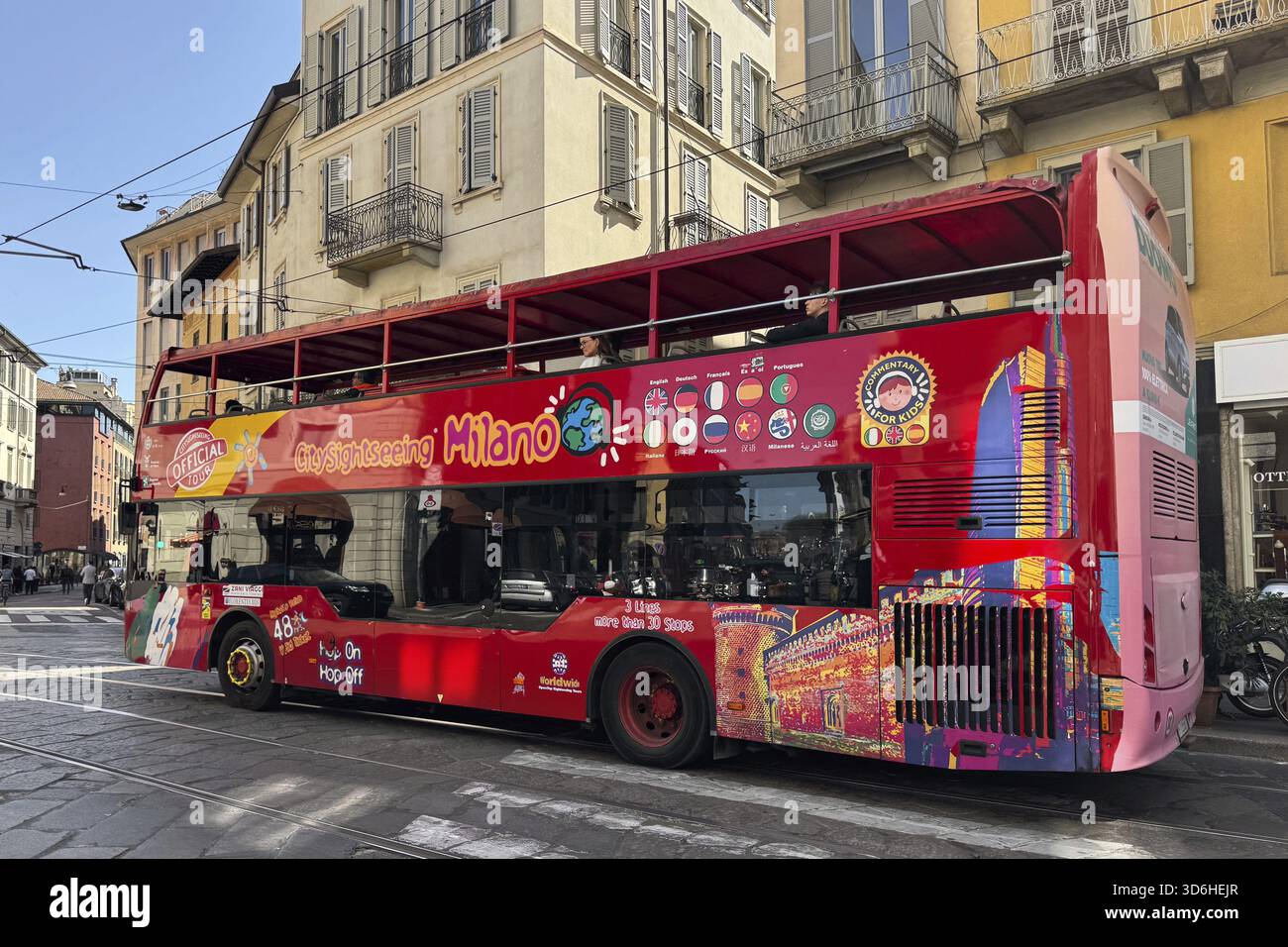 Milano, Italia - 11 aprile 2025: Autobus rosso City Sightseeing Milano con grafica colorata sulla strada vicino ai classici edifici gialli. Open TOP, storico cen Foto Stock