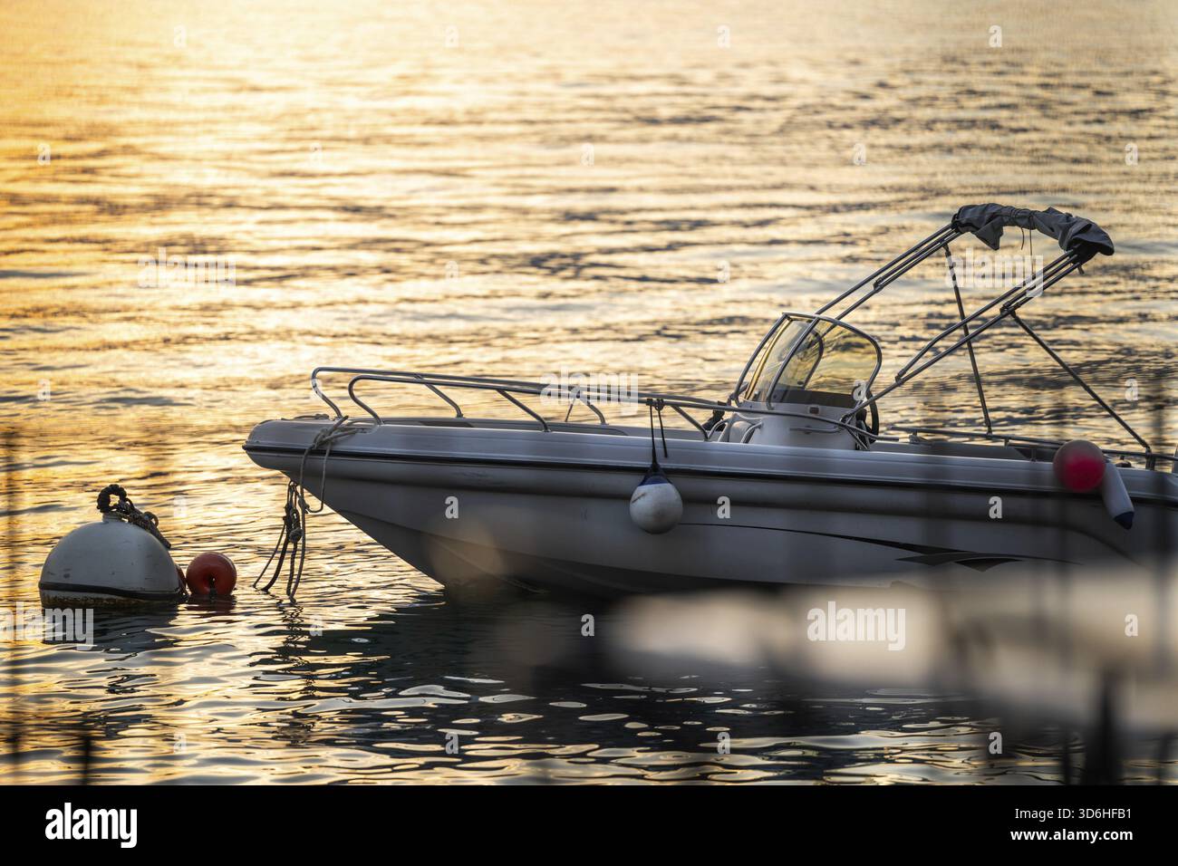 La barca galleggia pacificamente sull'acqua dorata durante il tramonto ancorata da boa. Il luogo perfetto per una serata tranquilla sul lago di Como, in Italia Foto Stock