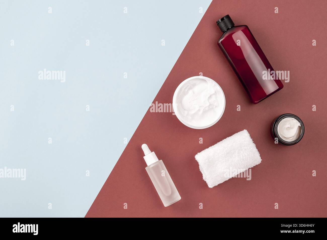 Prodotti per la cura della pelle su superfici marroni e blu. Cornice dal flacone di shampoo o lozione cosmetica, asciugamano, vaso panna aperto, siero con peptidi. Bellezza, spa co Foto Stock