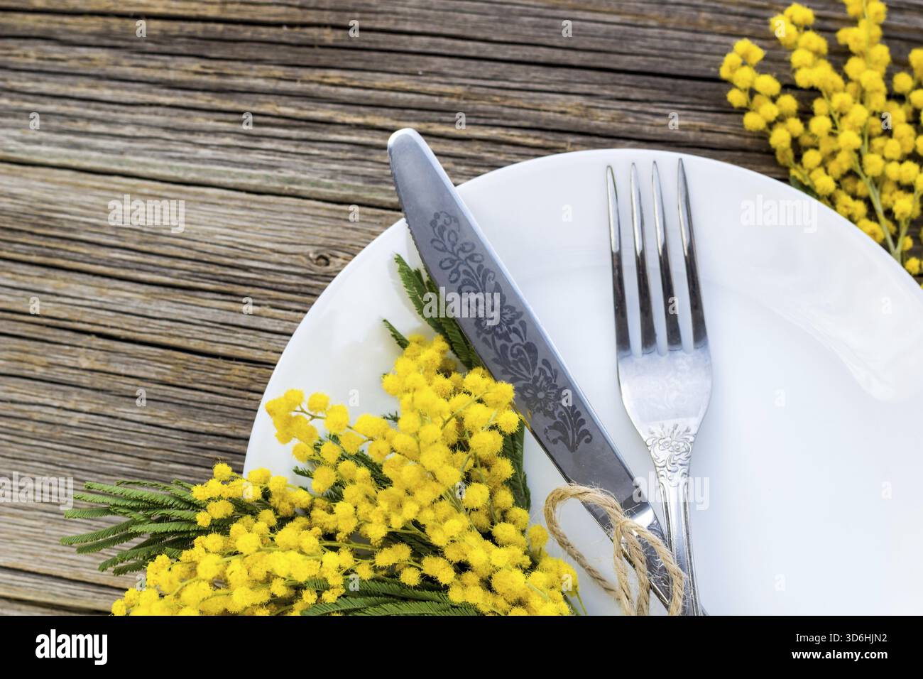 Cibo, coltello a forchetta con piatto e fiori di mimosa su un tavolo di legno per la cena delle vacanze di Pasqua di primavera. Vista dall'alto Foto Stock