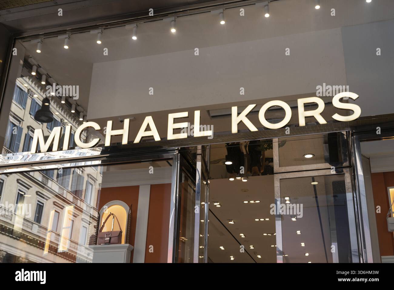 Milano, Italia - 8 aprile 2025: Ingresso al negozio Michael Kors con logo del marchio illuminato e esposizione di borse di lusso a Milano. Facciata boutique di moda Foto Stock