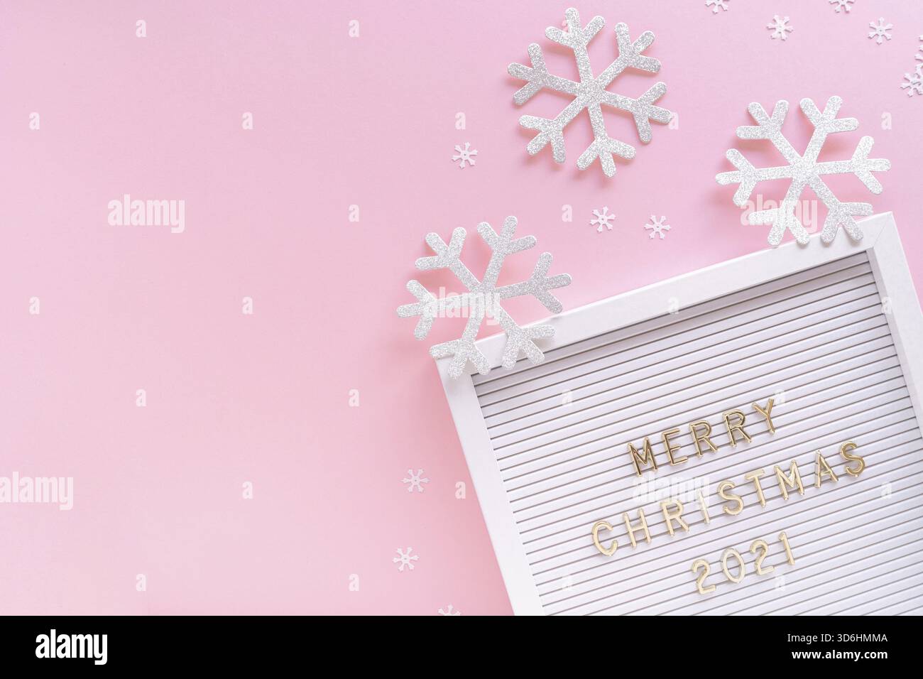Lavagna a lettere con auguri di buon Natale 2021, fiocco di neve decorativo su sfondo rosa pastello. Composizione della cornice natalizia. Posizione piatta, dall'alto Foto Stock