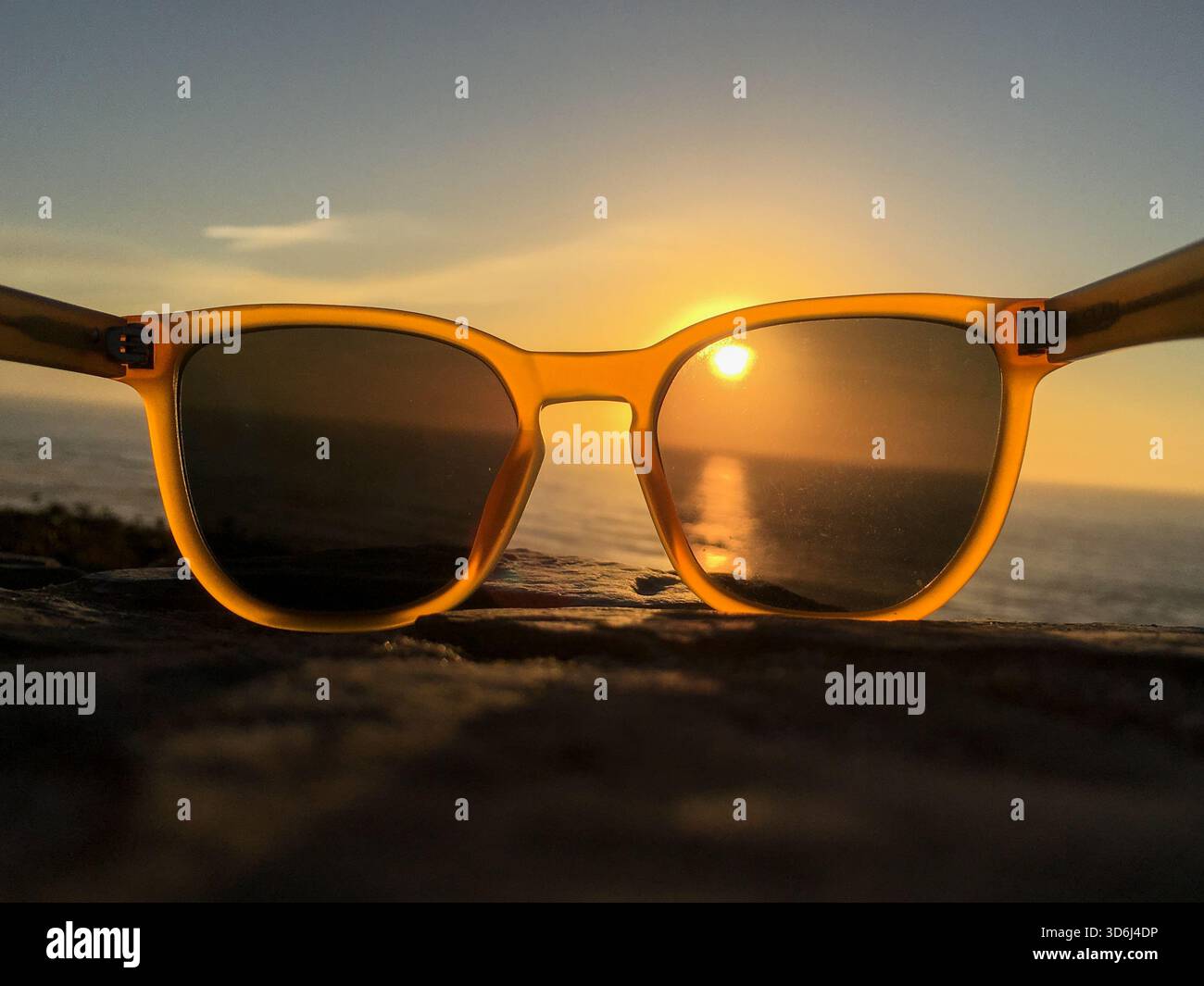 Primo piano di eleganti occhiali da sole posti all'aperto con splendida vista del tramonto sull'oceano. La luce dorata e soffusa crea un'atmosfera rilassata per l'estate e i viaggi. Foto Stock