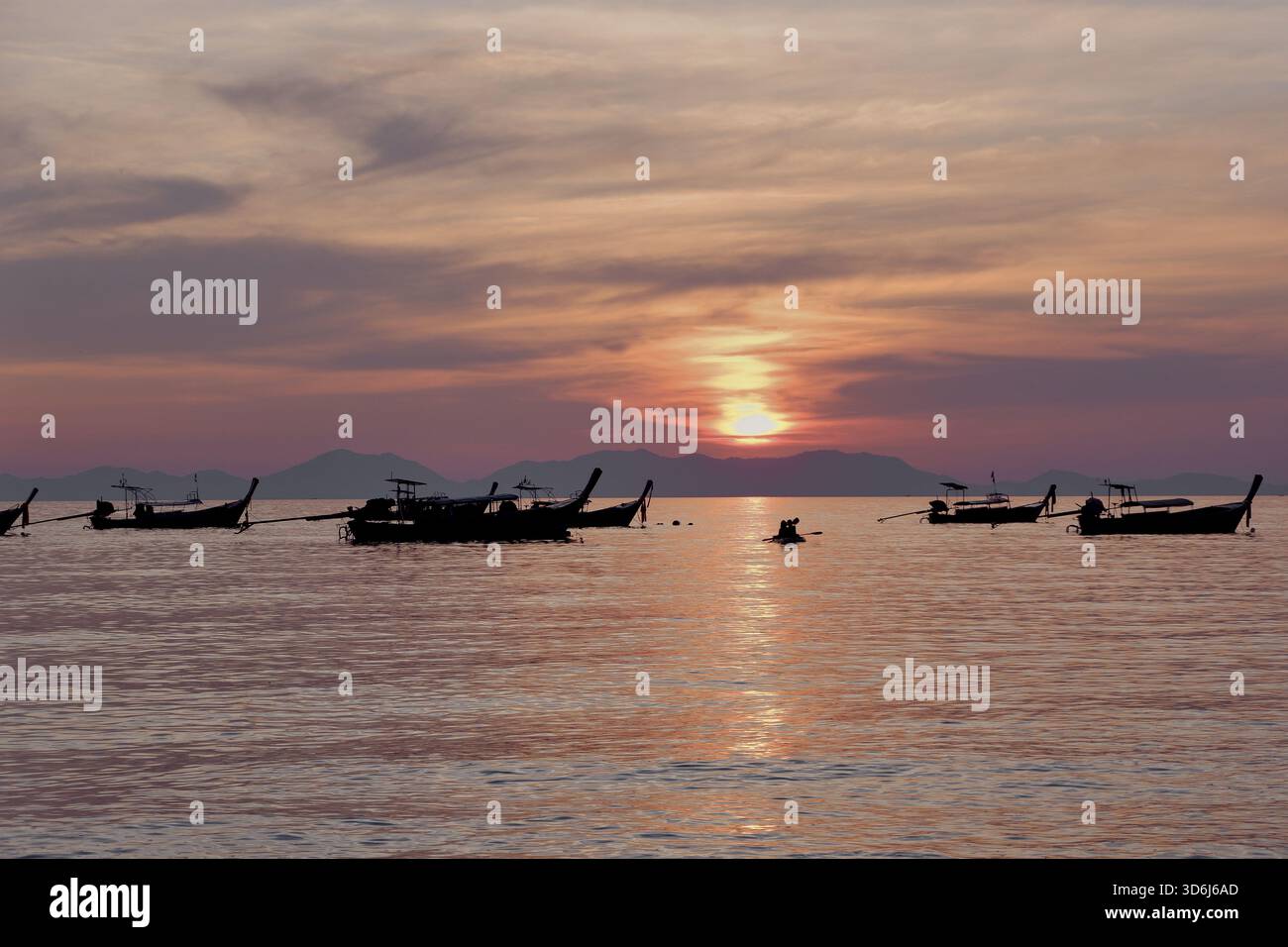 Un'ampia linea di barche galleggia vicino all'orizzonte mentre la luce dorata e le morbide nuvole riempiono il cielo, creando una scenografica scena di tramonto lungo l'acqua. Foto Stock