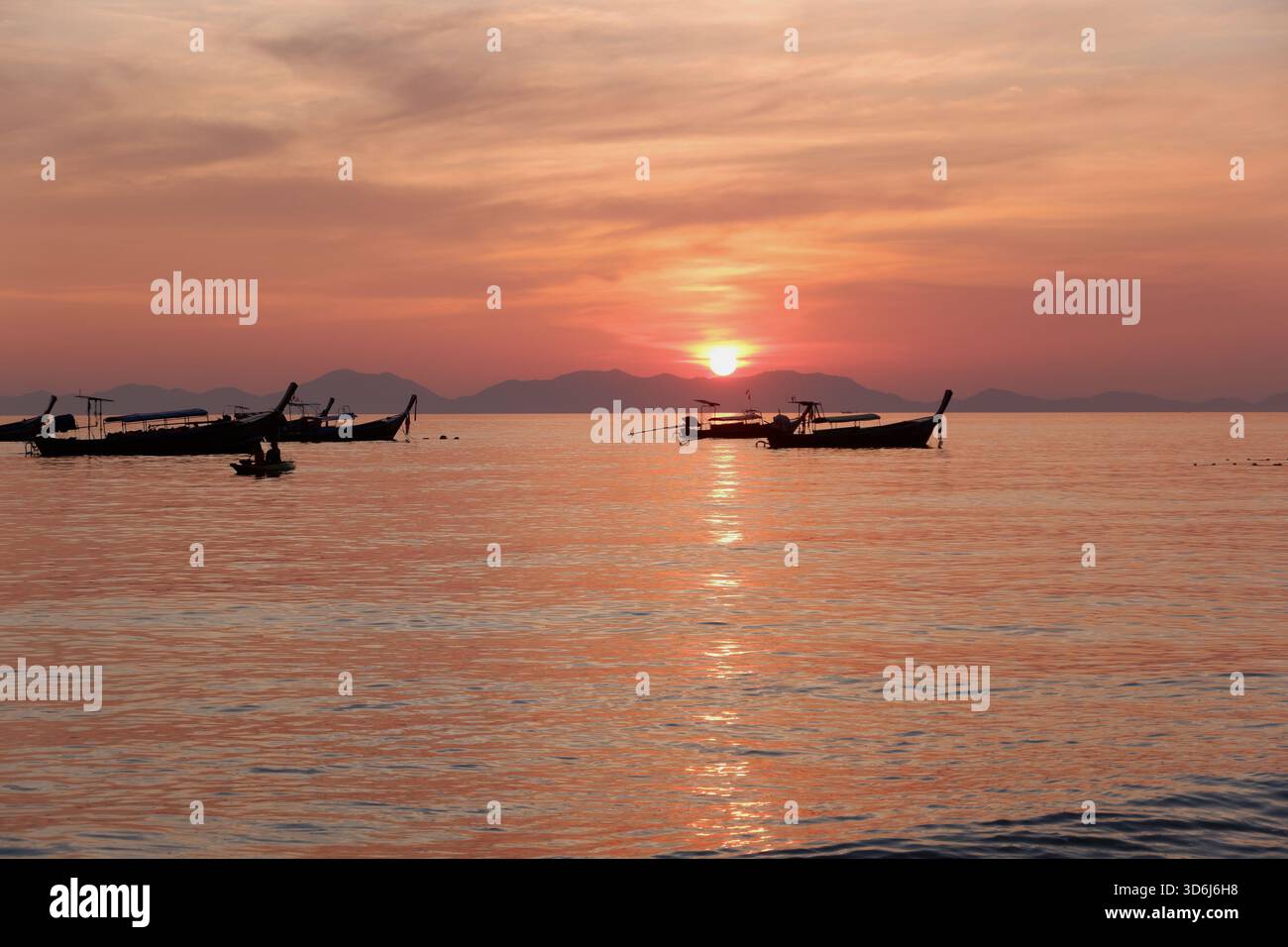 Una flotta di barche a coda lunga si estende sull'acqua mentre il sole si abbassa, dipingendo l'oceano e il cielo con sfumature di arancione e rosa. Foto Stock