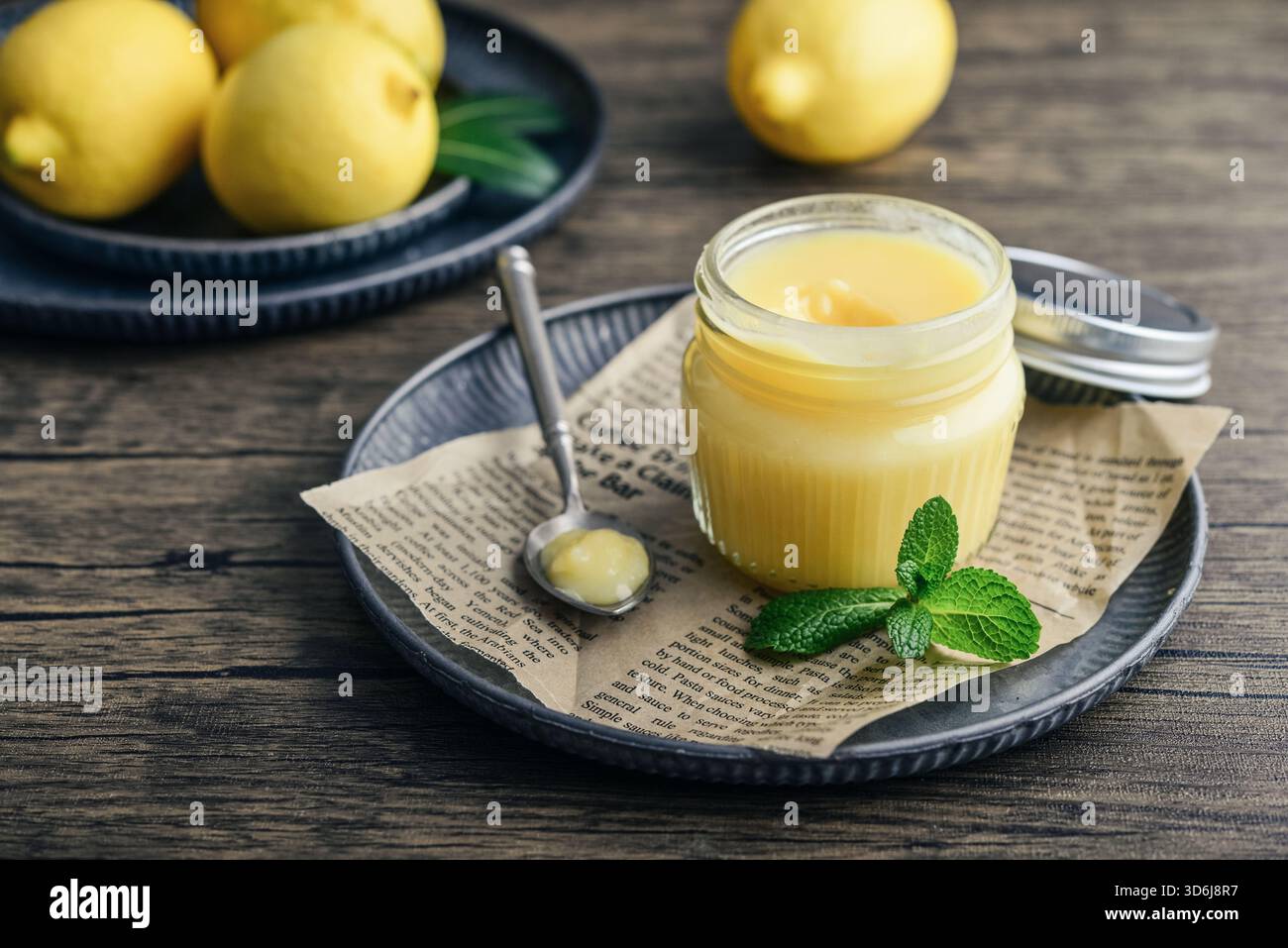 Cagliata di limone fatta in casa in un vaso di vetro con foglie di menta e limoni freschi su fondo di legno Foto Stock