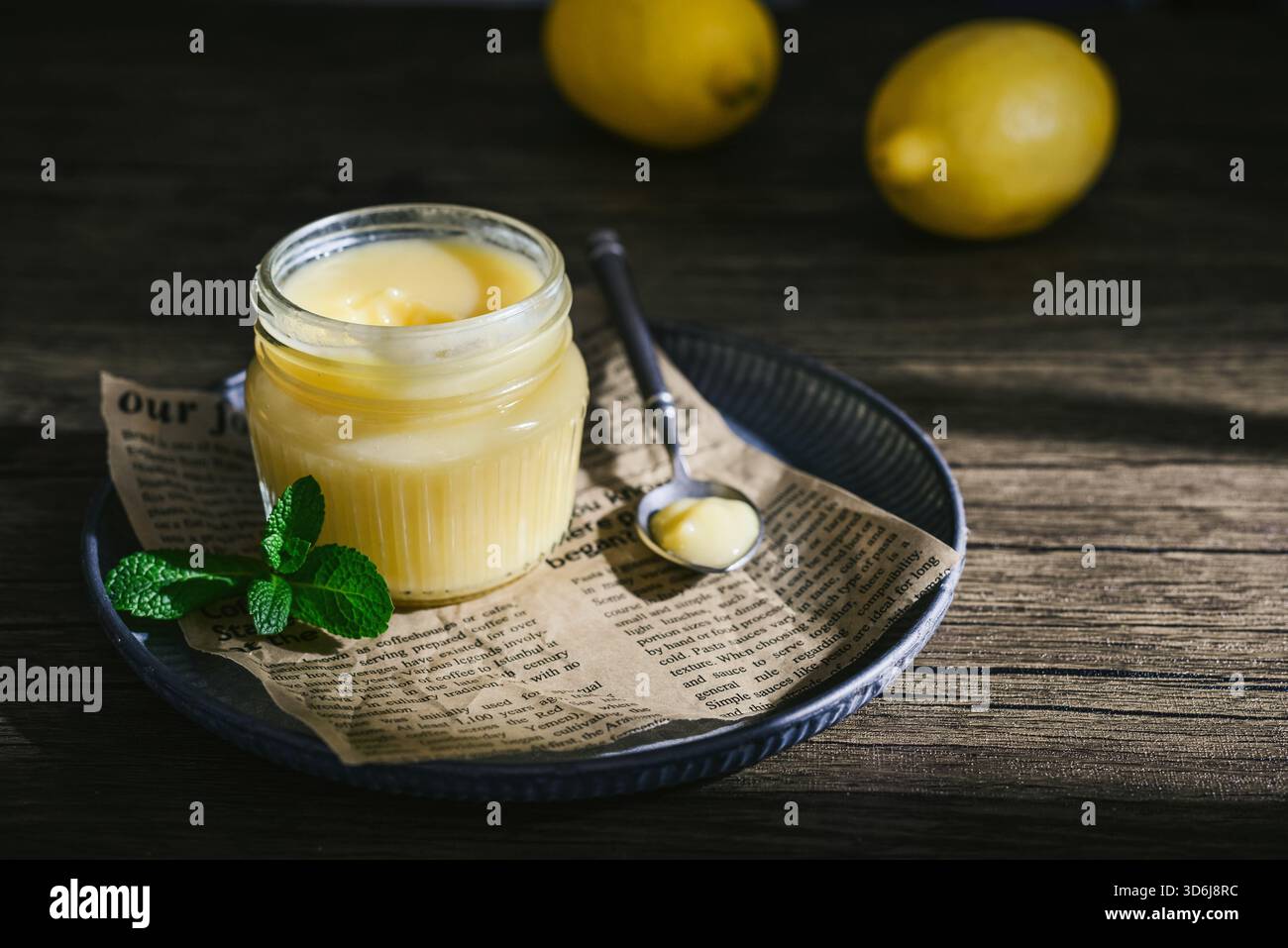 Cagliata di limone fatta in casa in un vaso di vetro con foglie di menta e limoni freschi su fondo di legno Foto Stock