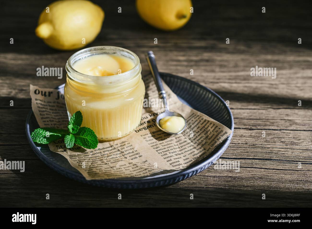 Cagliata di limone fatta in casa in un vaso di vetro con foglie di menta e limoni freschi su fondo di legno Foto Stock
