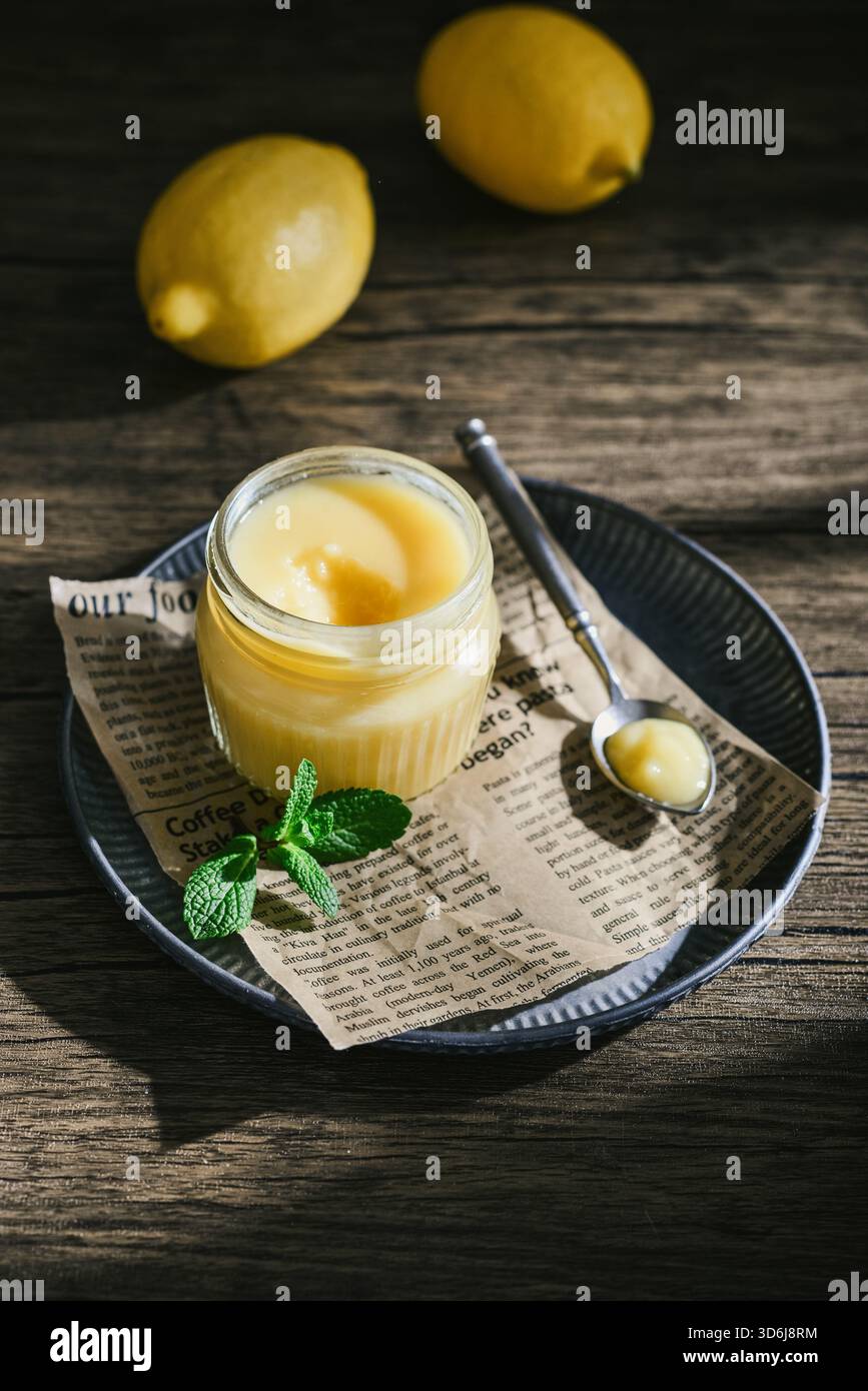 Cagliata di limone fatta in casa in un vaso di vetro con foglie di menta e limoni freschi su fondo di legno Foto Stock