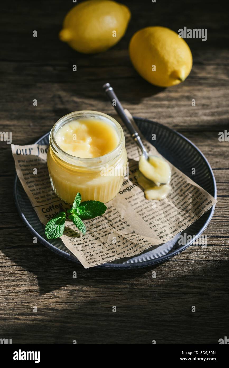Cagliata di limone fatta in casa in un vaso di vetro con foglie di menta e limoni freschi su fondo di legno Foto Stock