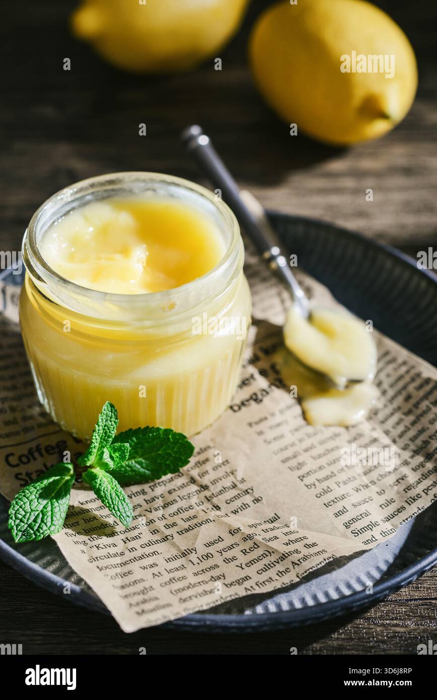 Cagliata di limone fatta in casa in un vaso di vetro con foglie di menta e limoni freschi su fondo di legno Foto Stock