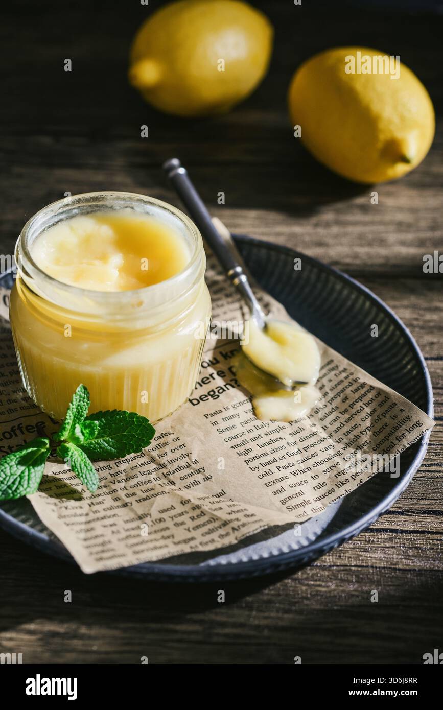 Cagliata di limone fatta in casa in un vaso di vetro con foglie di menta e limoni freschi su fondo di legno Foto Stock