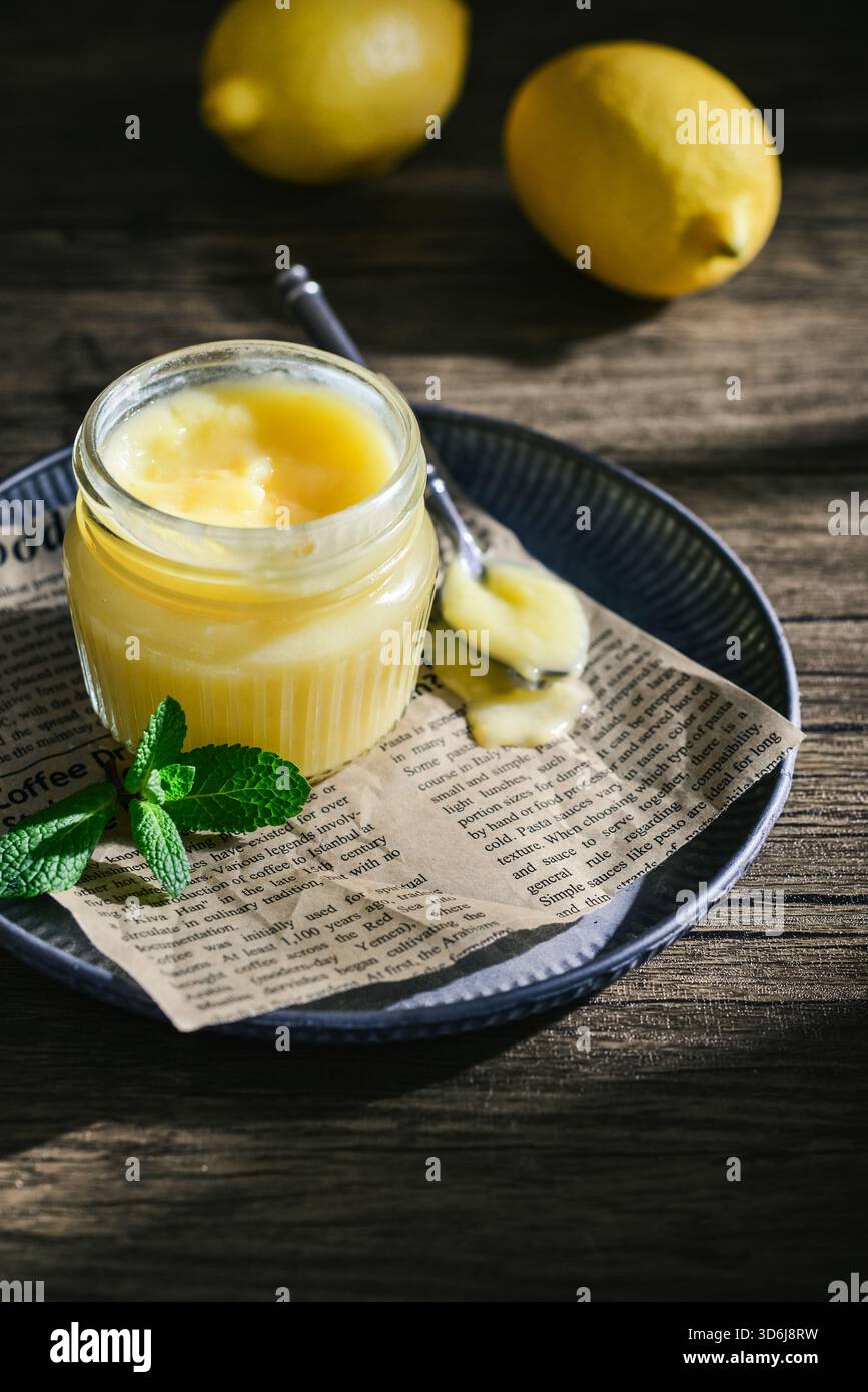 Cagliata di limone fatta in casa in un vaso di vetro con foglie di menta e limoni freschi su fondo di legno Foto Stock