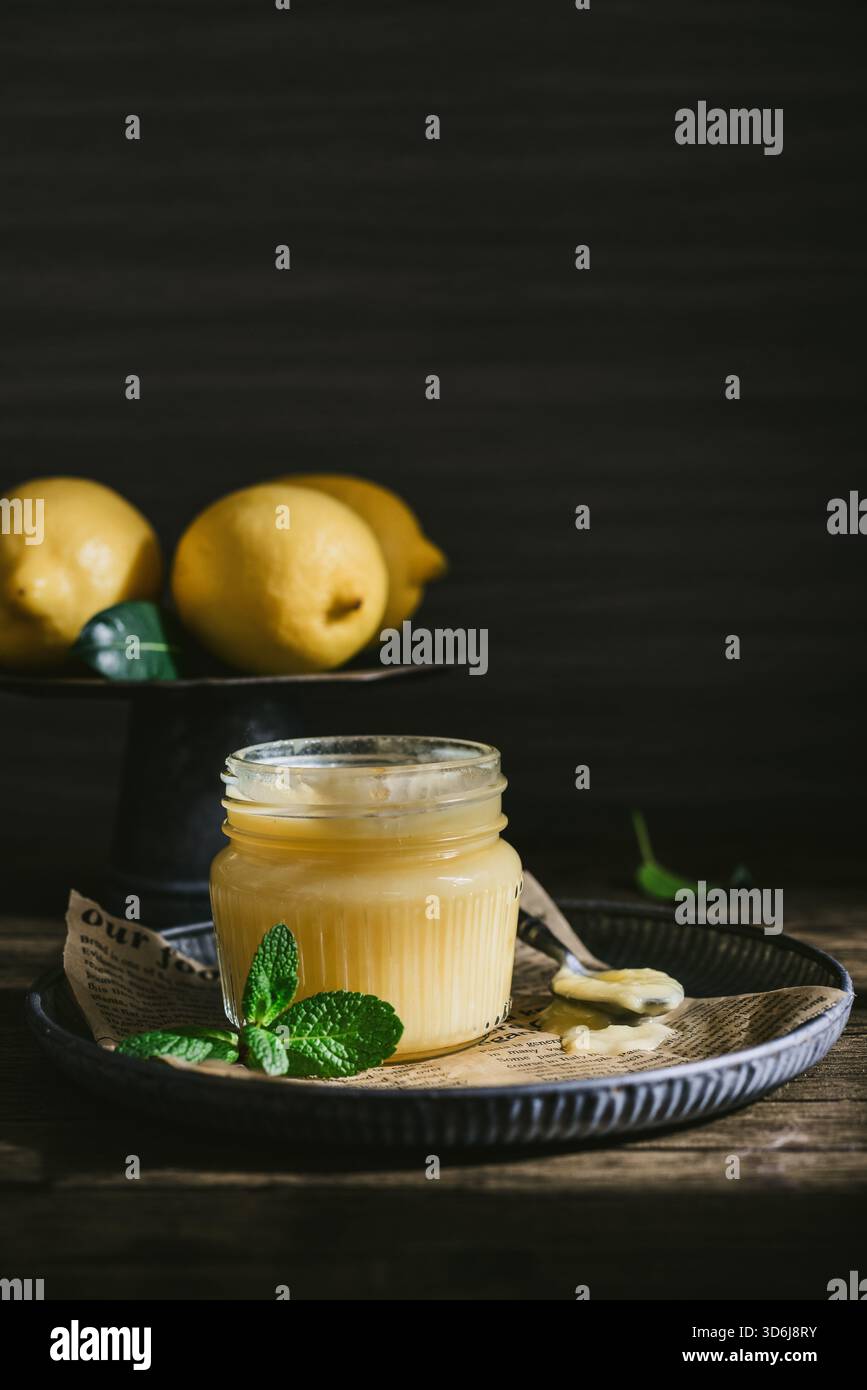 Cagliata di limone fatta in casa in un vaso di vetro con foglie di menta e limoni freschi su fondo di legno Foto Stock