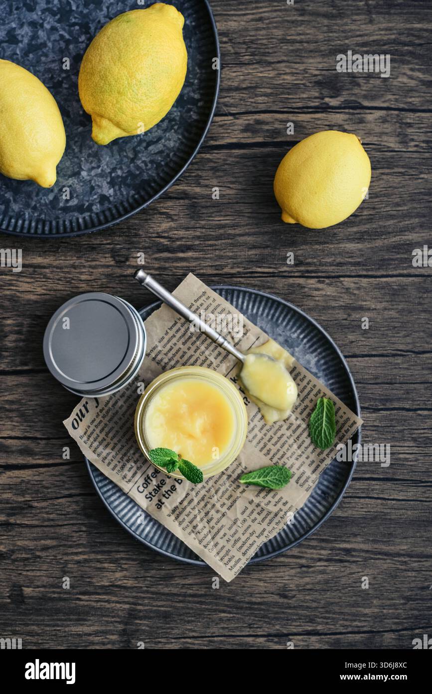 Cagliata di limone fatta in casa in un vaso di vetro con foglie di menta e limoni freschi su sfondo di legno, vista dall'alto Foto Stock