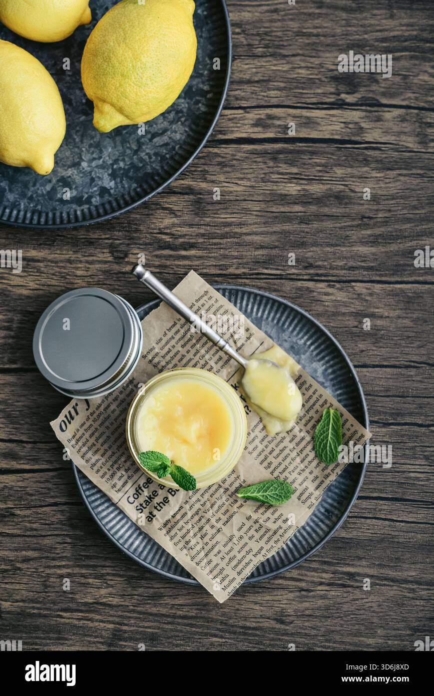 Cagliata di limone fatta in casa in un vaso di vetro con foglie di menta e limoni freschi su sfondo di legno, vista dall'alto Foto Stock