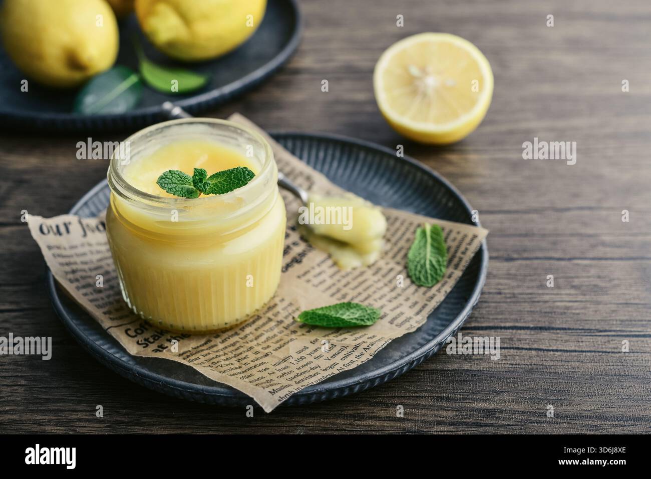 Cagliata di limone fatta in casa in un vaso di vetro con foglie di menta e limoni freschi su fondo di legno Foto Stock