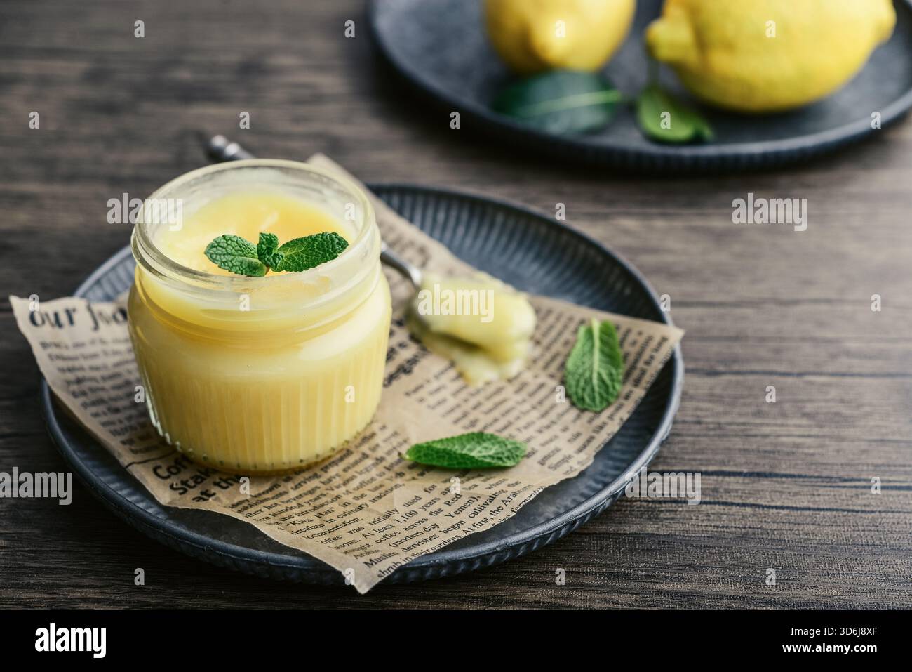 Cagliata di limone fatta in casa in un vaso di vetro con foglie di menta e limoni freschi su fondo di legno Foto Stock