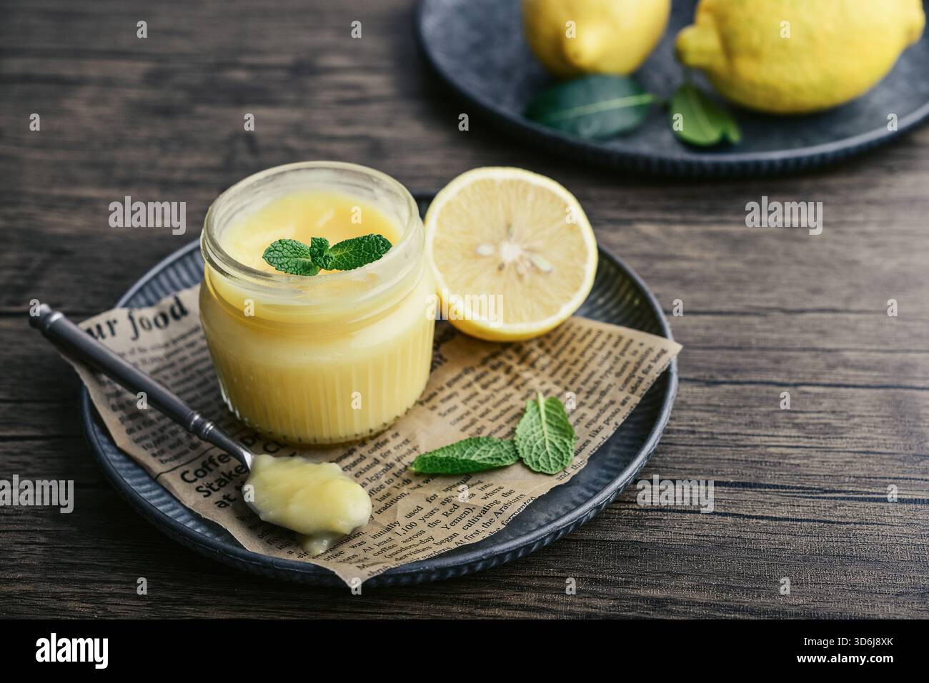 Cagliata di limone fatta in casa in un vaso di vetro con foglie di menta e limoni freschi su fondo di legno Foto Stock