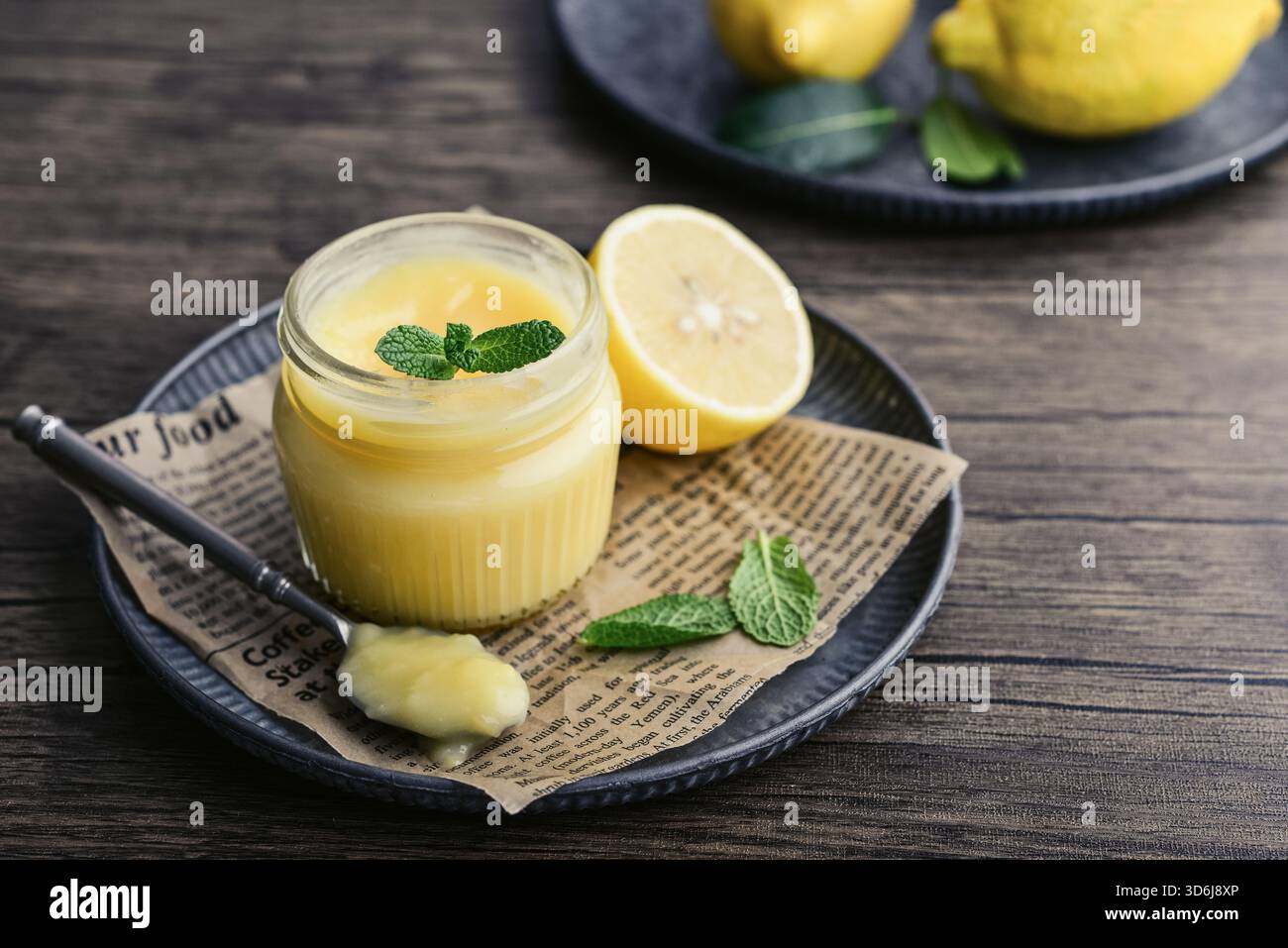 Cagliata di limone fatta in casa in un vaso di vetro con foglie di menta e limoni freschi su fondo di legno Foto Stock