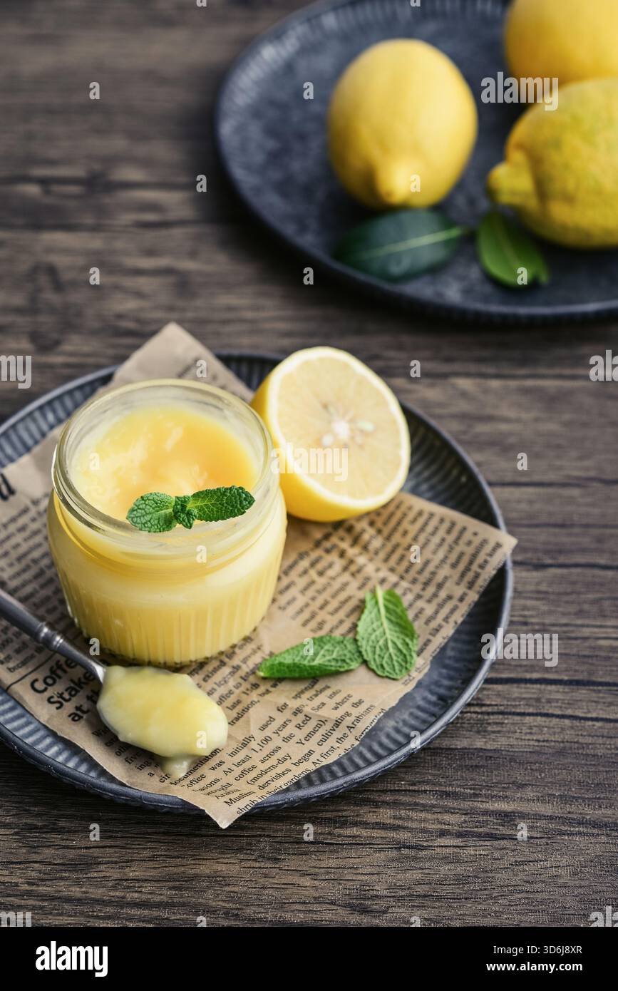 Cagliata di limone fatta in casa in un vaso di vetro con foglie di menta e limoni freschi su fondo di legno Foto Stock