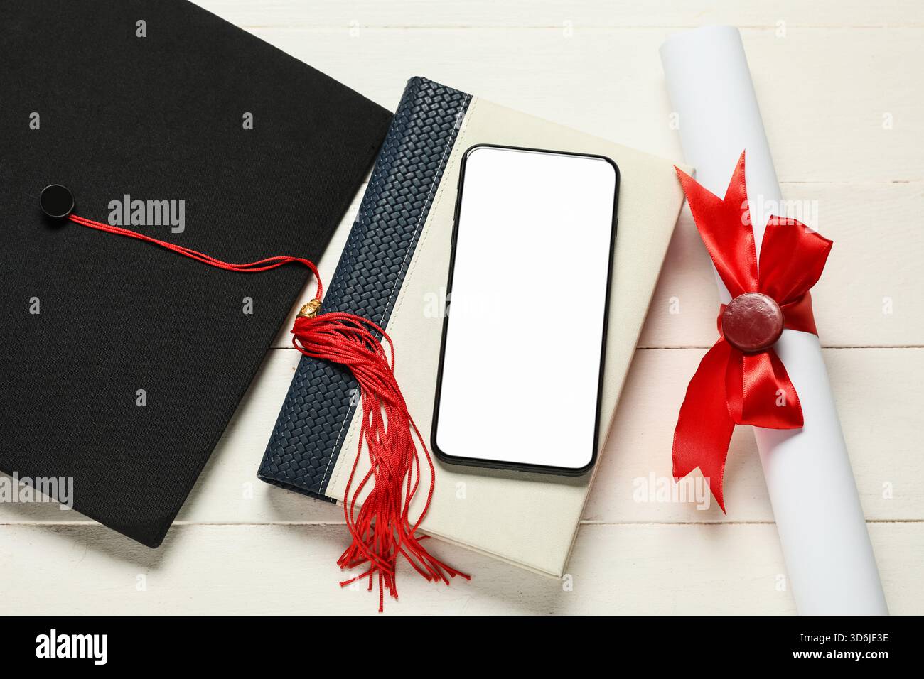 Cappello di laurea, libro, telefono cellulare e diploma su sfondo bianco in legno, vista dall'alto Foto Stock