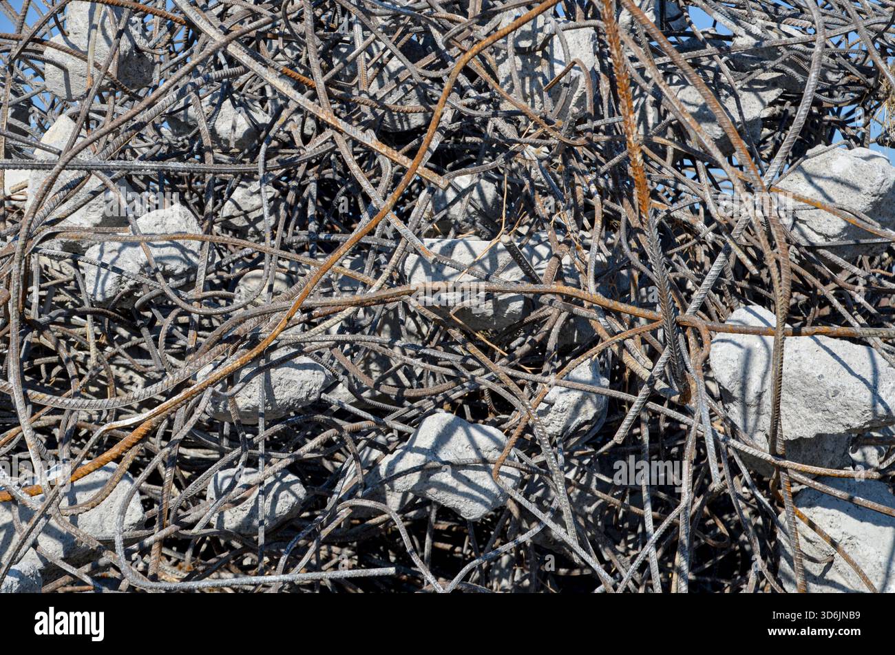 Primo piano dettagliato di tondini arrugginiti e arrugginiti (acciaio di rinforzo) mescolati con frammenti di macerie di cemento, raccolti per il riciclaggio. Foto Stock
