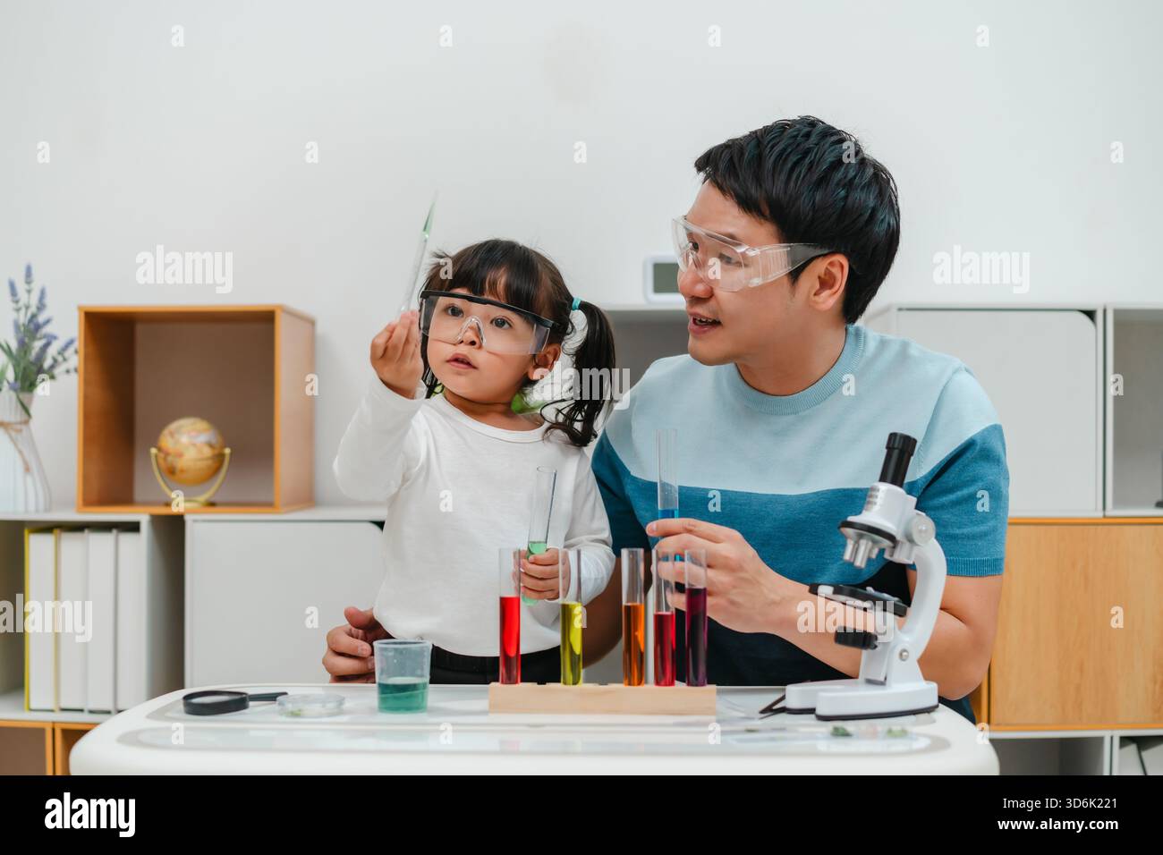 studio scientifico della bambina con l'utilizzo del liquido contagocce per pipette con provetta e becher. imparando la scienza con suo padre Foto Stock