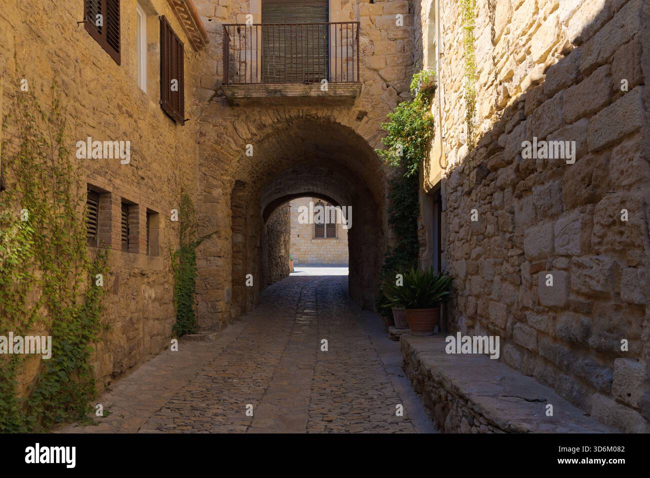 Stretta strada acciottolata nel centro storico di Peratallada, passando sotto arcate in pietra con mura rustiche e piante da arrampicata. Foto Stock