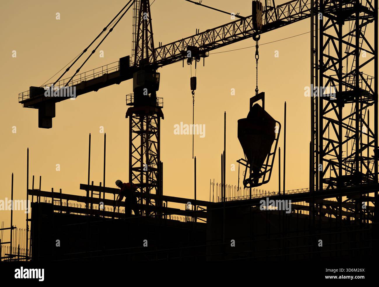 Costruendo il futuro, scendi dal sito di costruzione di un moderno e alto edificio con gru e macchinari pesanti in silhouette Foto Stock
