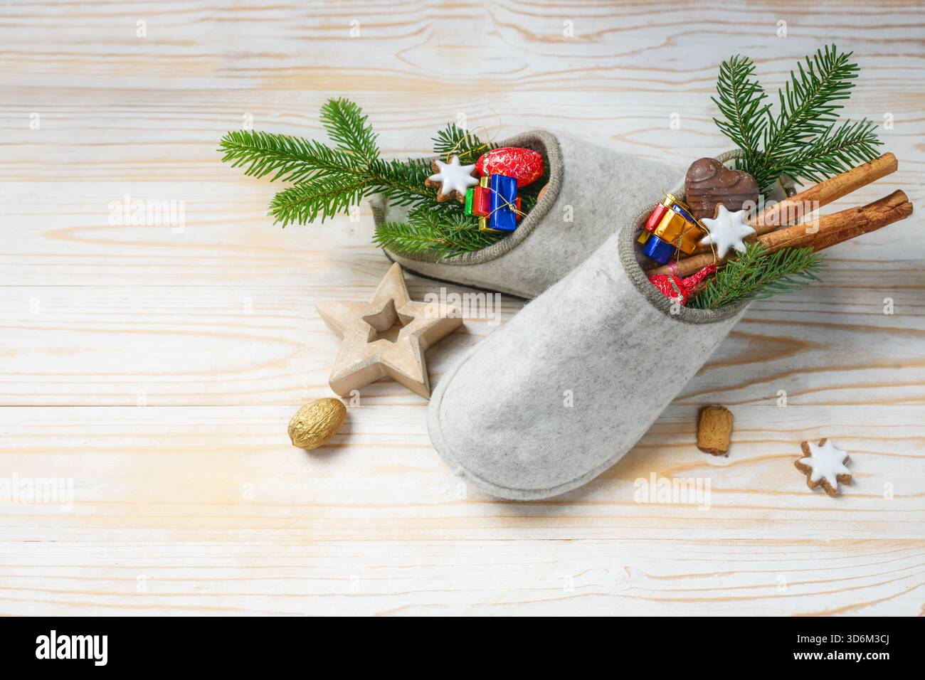 6 dicembre, festa tedesca Nikolaus Tag o giorno di San Nicola, pantofole in feltro piene di dolci e decorazioni natalizie su un pavimento di legno chiaro, copia Foto Stock