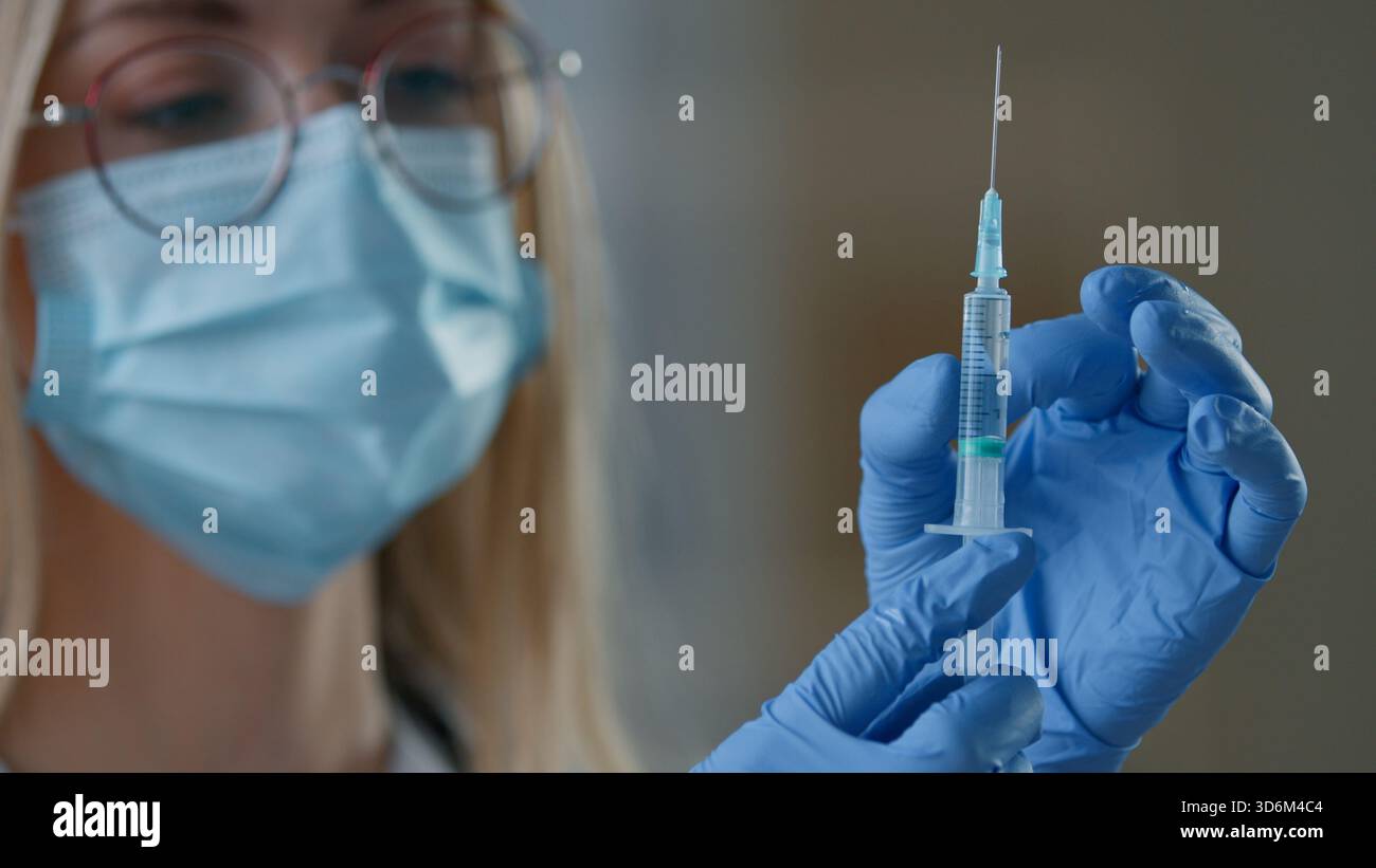 Primo piano donna caucasica medico in maschera medica che tiene siringa iniezione vaccinazione in clinica infermiera ragazza donna che si prepara per il rimedio vaccino Foto Stock