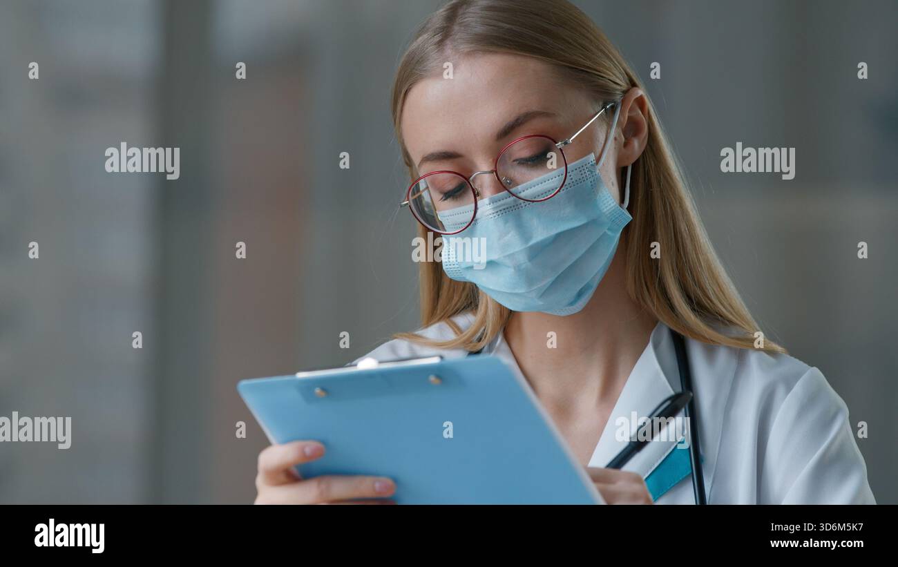 Donna caucasica medico infermiera in maschera di scrittura in carta medica pensando ragazza pensiva femminile in ospedale clinica scrivere informazioni pensare diagnosi Foto Stock