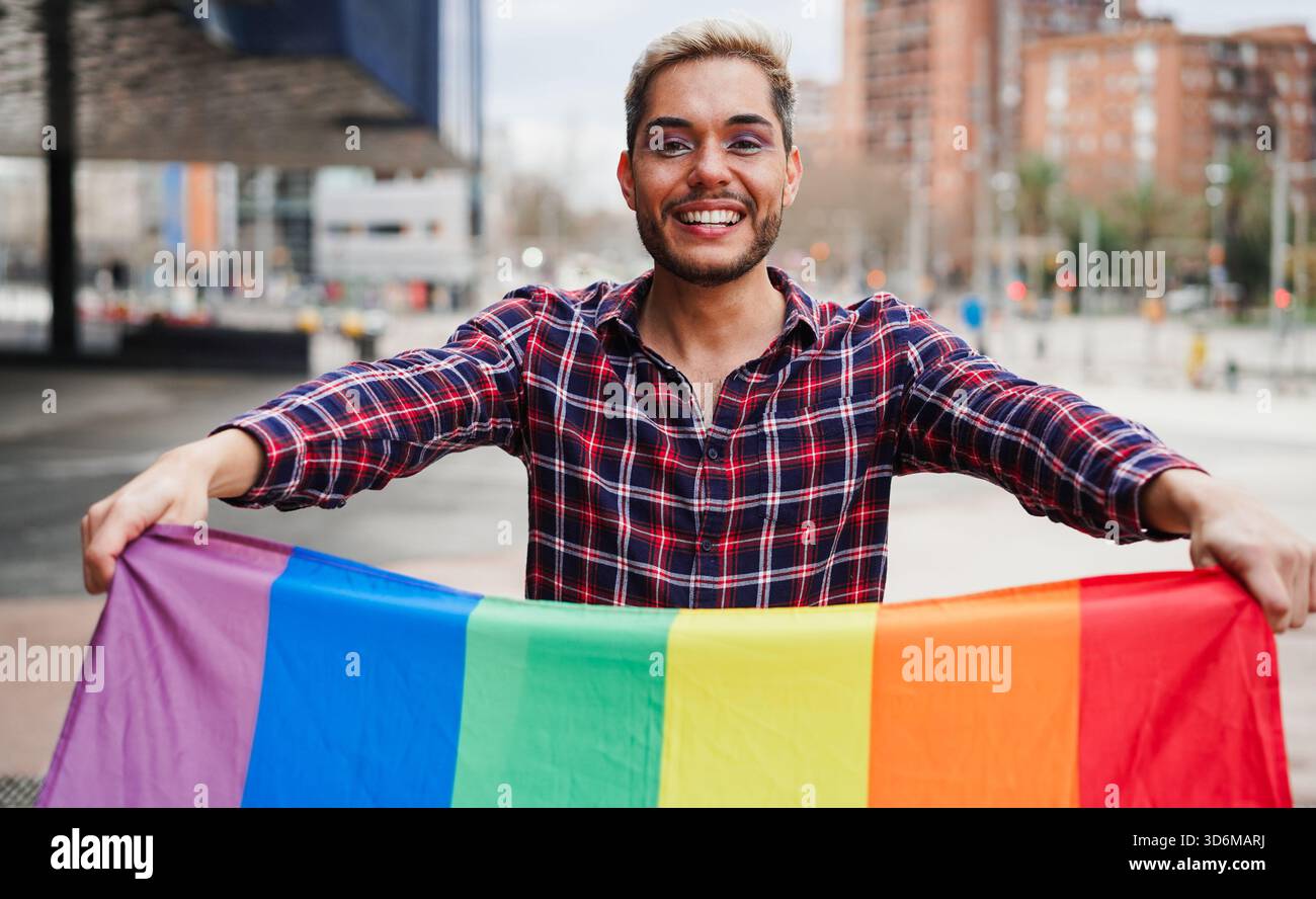 Giovane uomo gay con trucco per divertirsi tenendo la bandiera arcobaleno lgbt all'aperto - pari diritti per le persone omosessuali e concetto lgbtq - Focus on Face Foto Stock