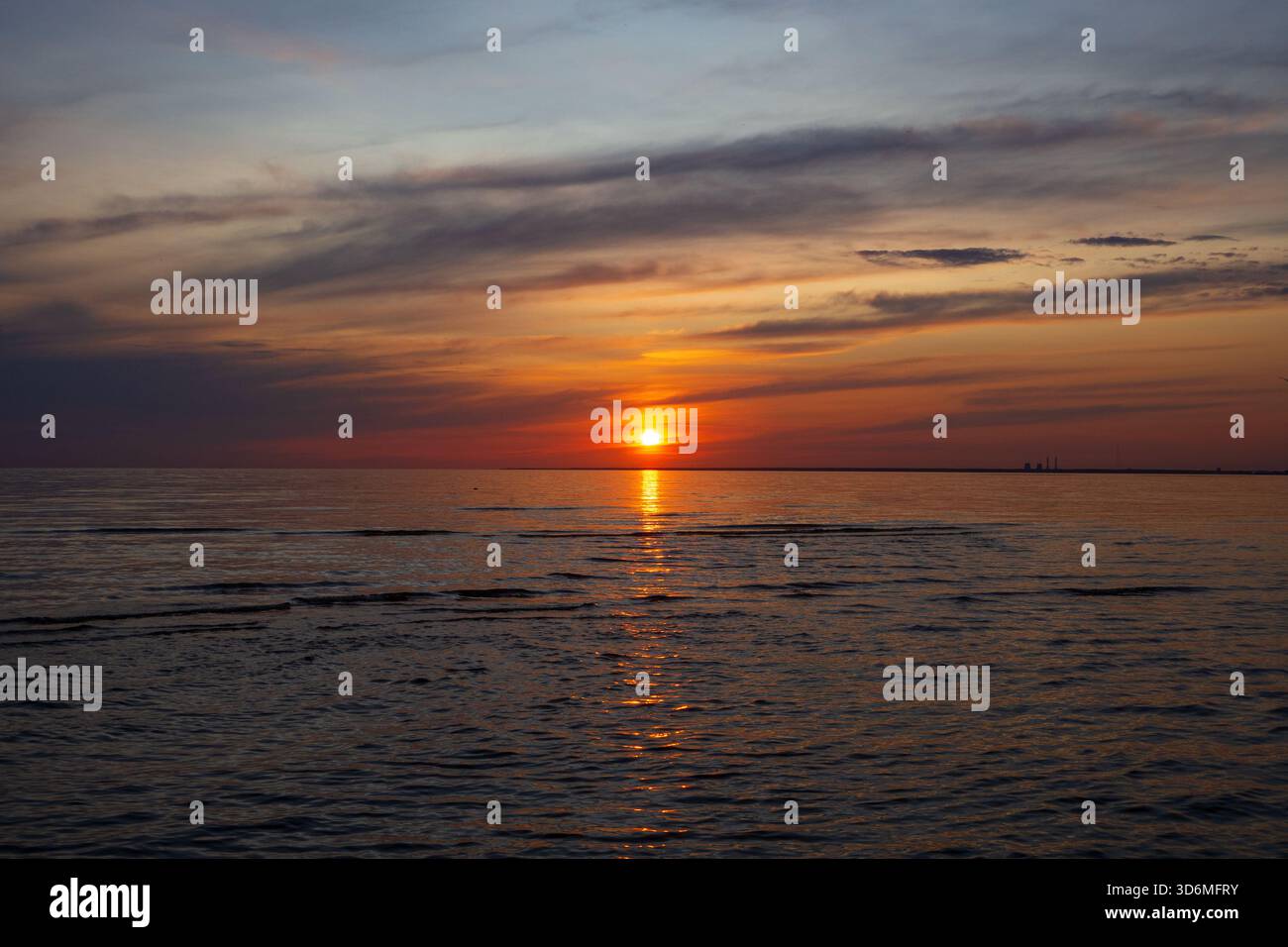 Un tramonto sereno proietta calde sfumature arancioni e rosse sul cielo e sull'acqua. Onde delicate riflettono la luce del sole che svanisce sull'orizzonte tranquillo. Golden Hou Foto Stock