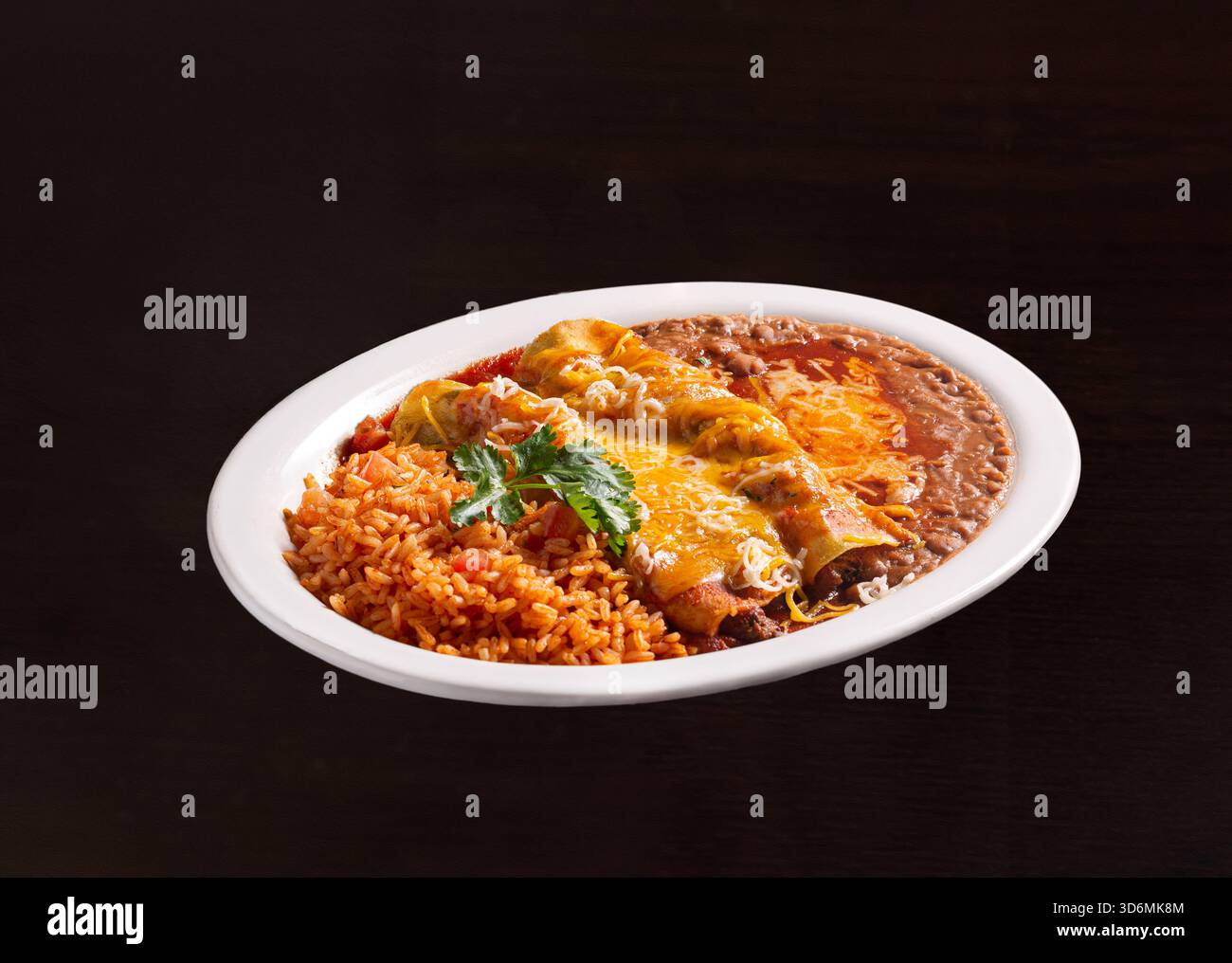 Ampio piatto di enchilada con riso rosso e fagioli fritti ricoperti di formaggio fuso Foto Stock