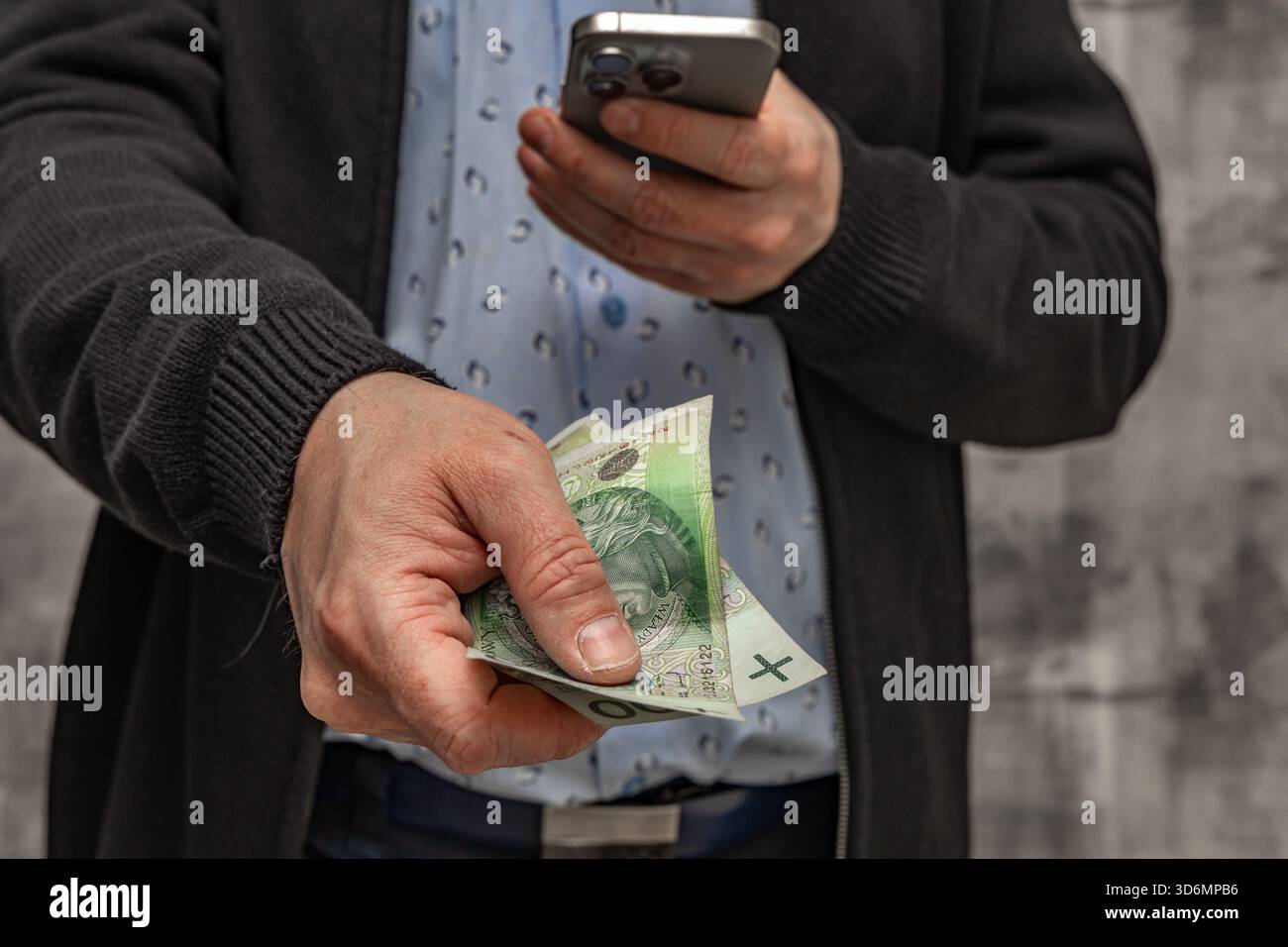 Un uomo con una camicia blu e un maglione tiene i soldi in mano, contando i soldi prima di spenderli. Foto Stock
